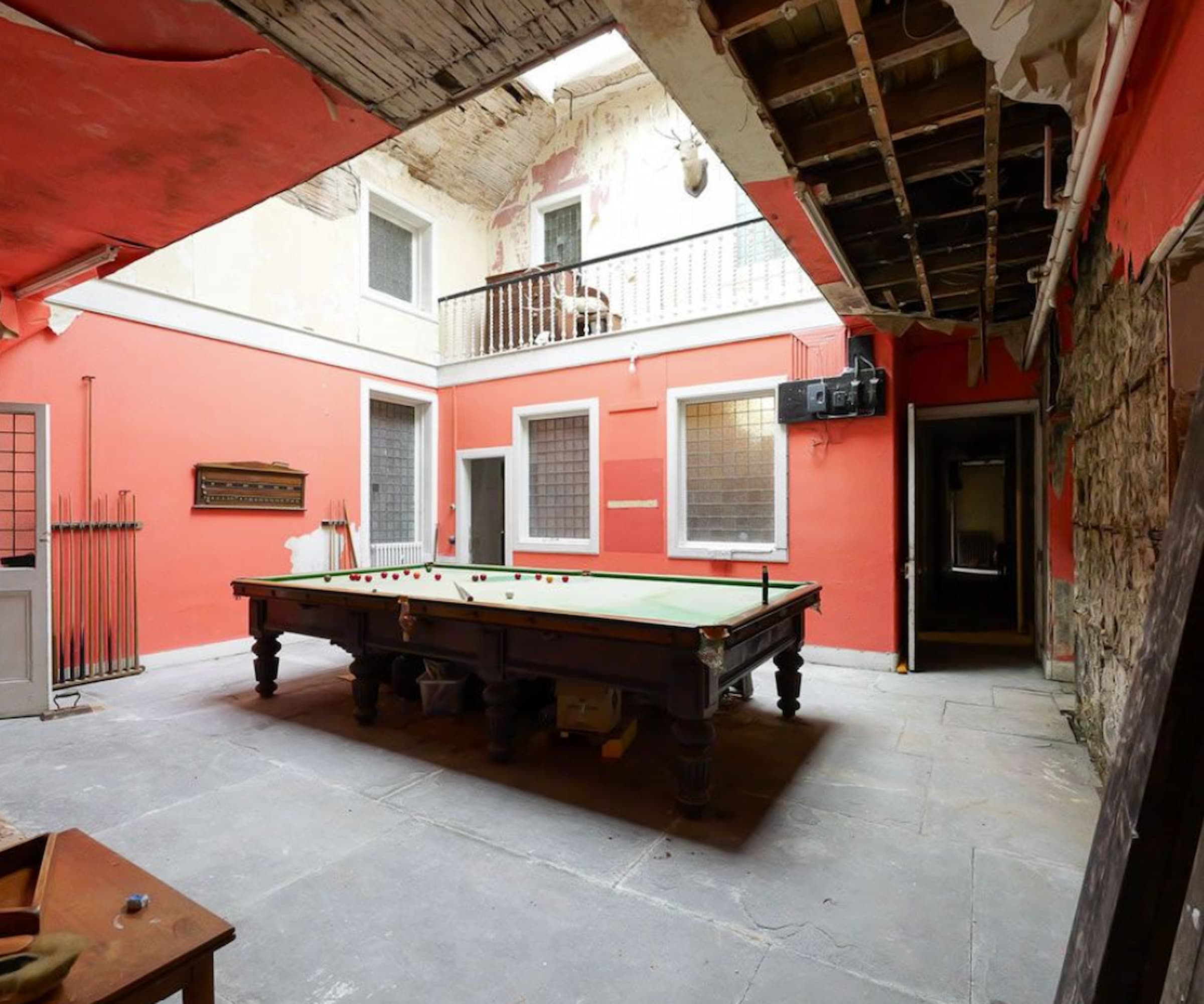 A games room in disrepair with bare walls and a snooker table
