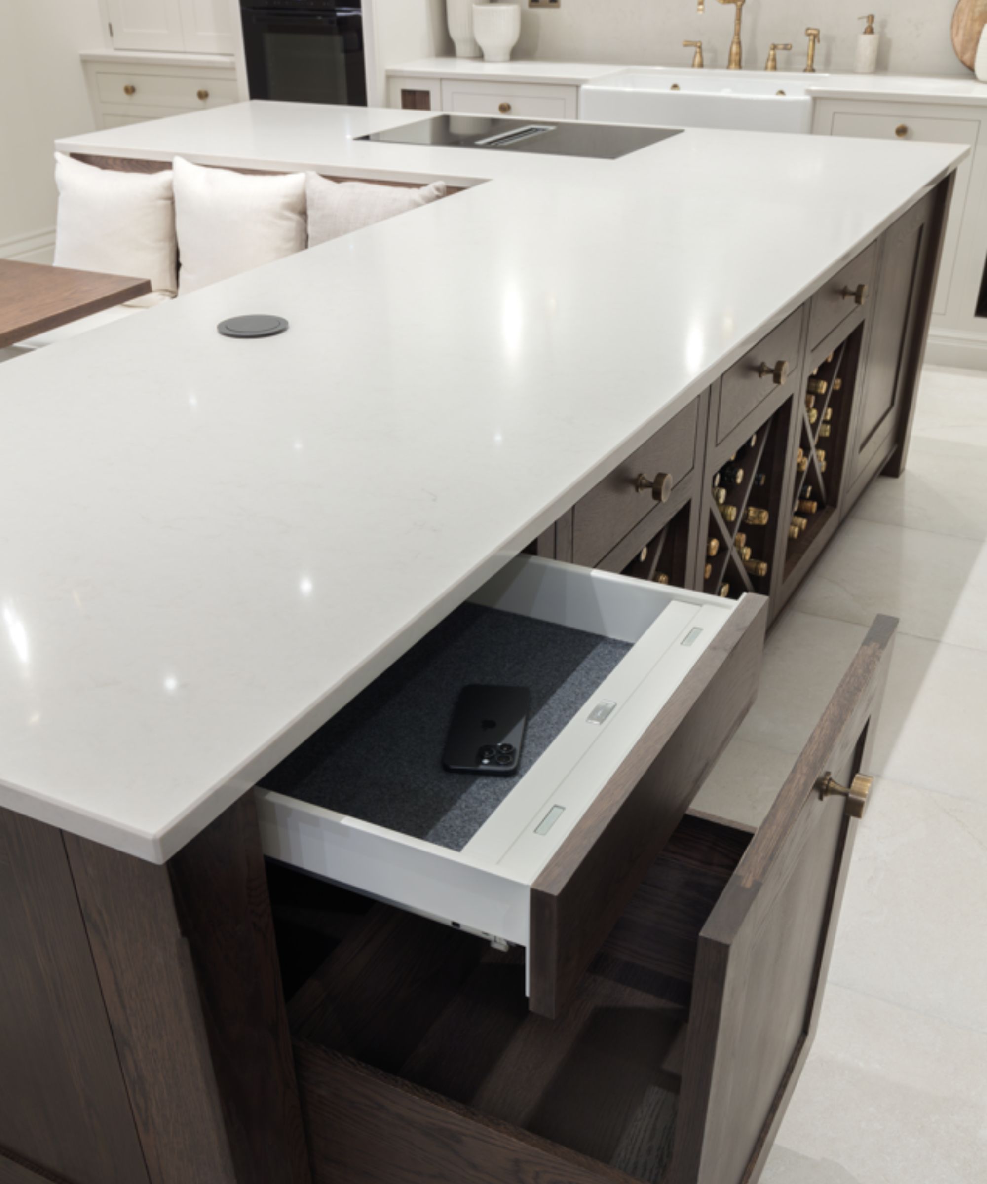 A sleek kitchen island features a pull-out drawer with a hidden safe inside, holding a smartphone.