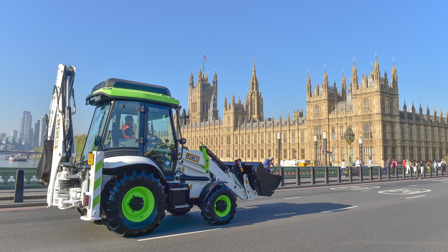 A green digger with the Houses of Parliament in the background -  the government has changed the law to give hydrogen diggers the green light to be driven on UK roads.