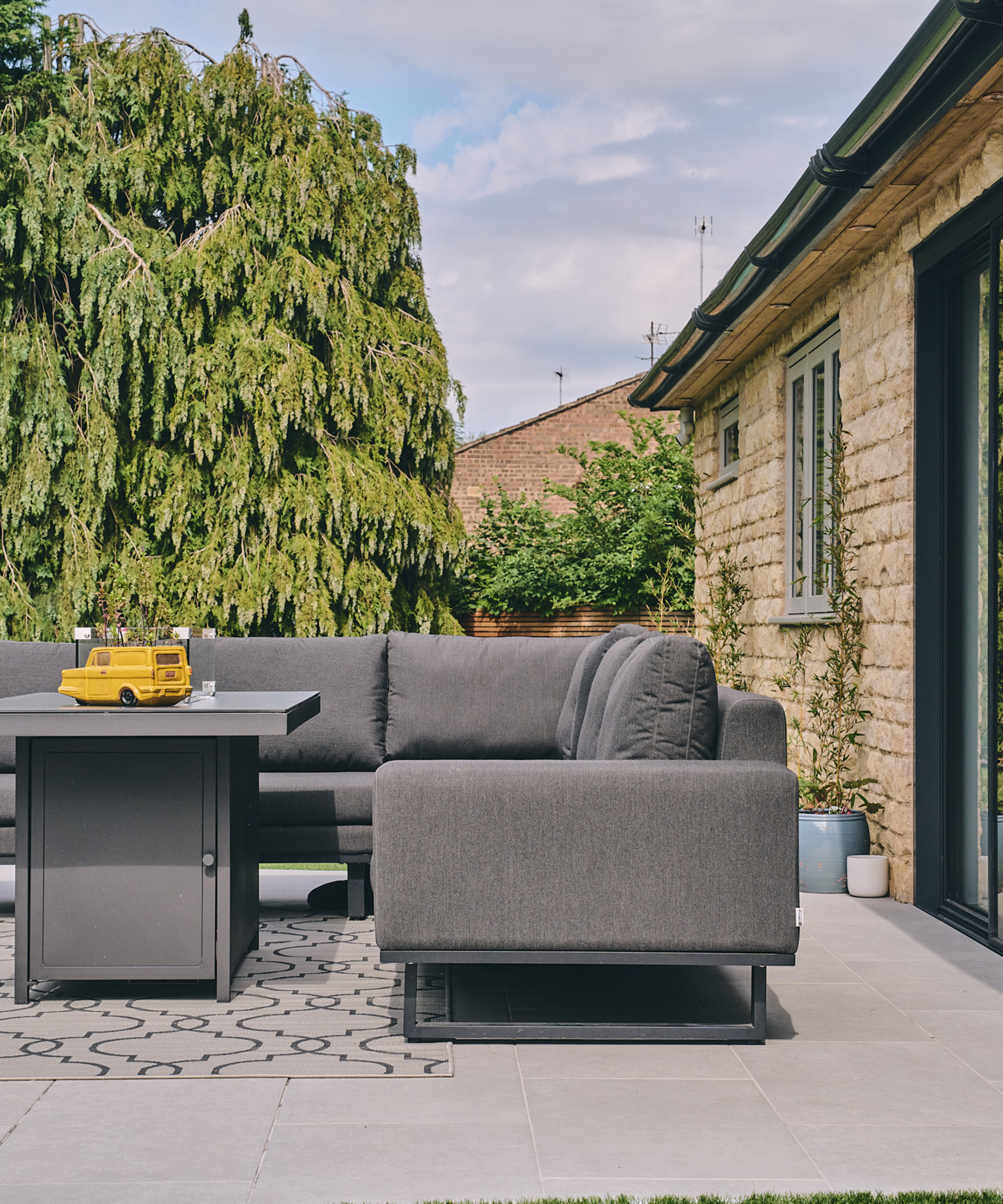 Grey outdoor corner sofa on a patio with tree in the background