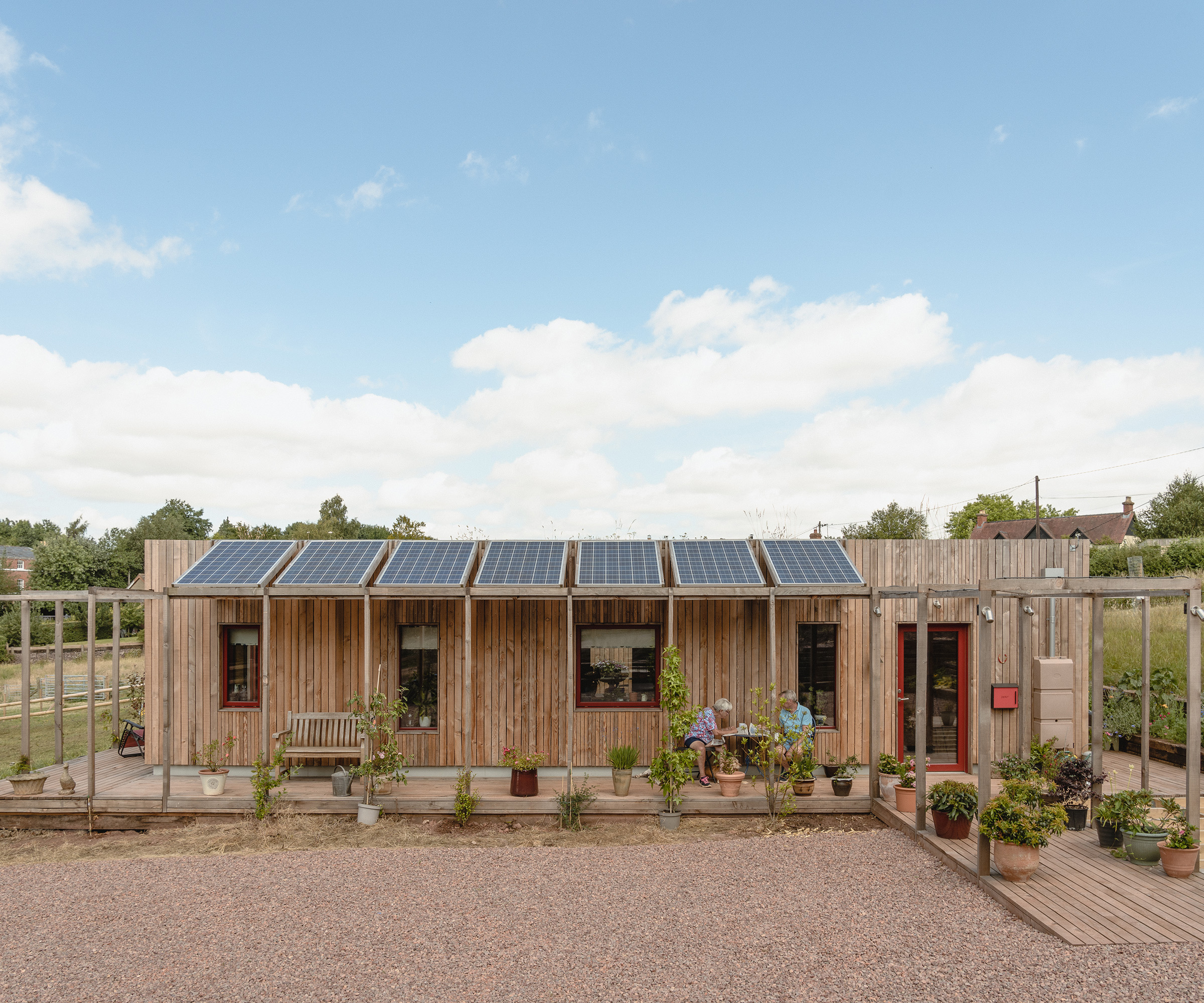 Couple sits outside their single storey self build home made from a modular timber construction system