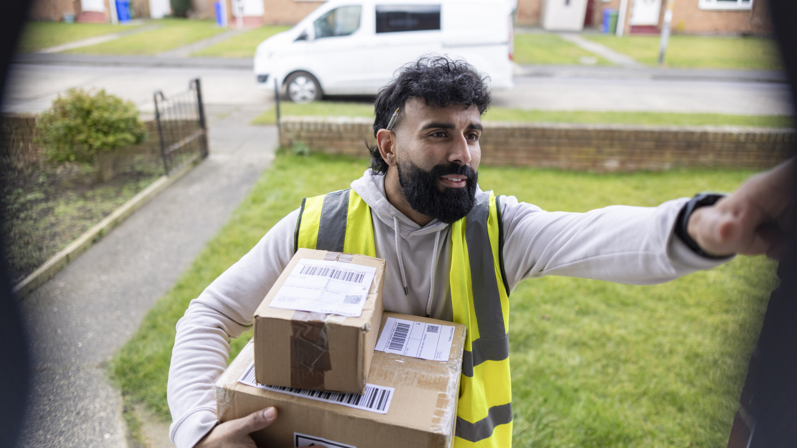 Delivery driver standing on the doorstep of a house, holding a package while pressing a smart doorbell camera