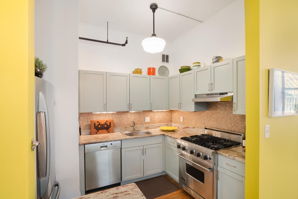 small kitchen with white cabinets and stainless steel appliances and hardwood floors and pendant light after renovation
