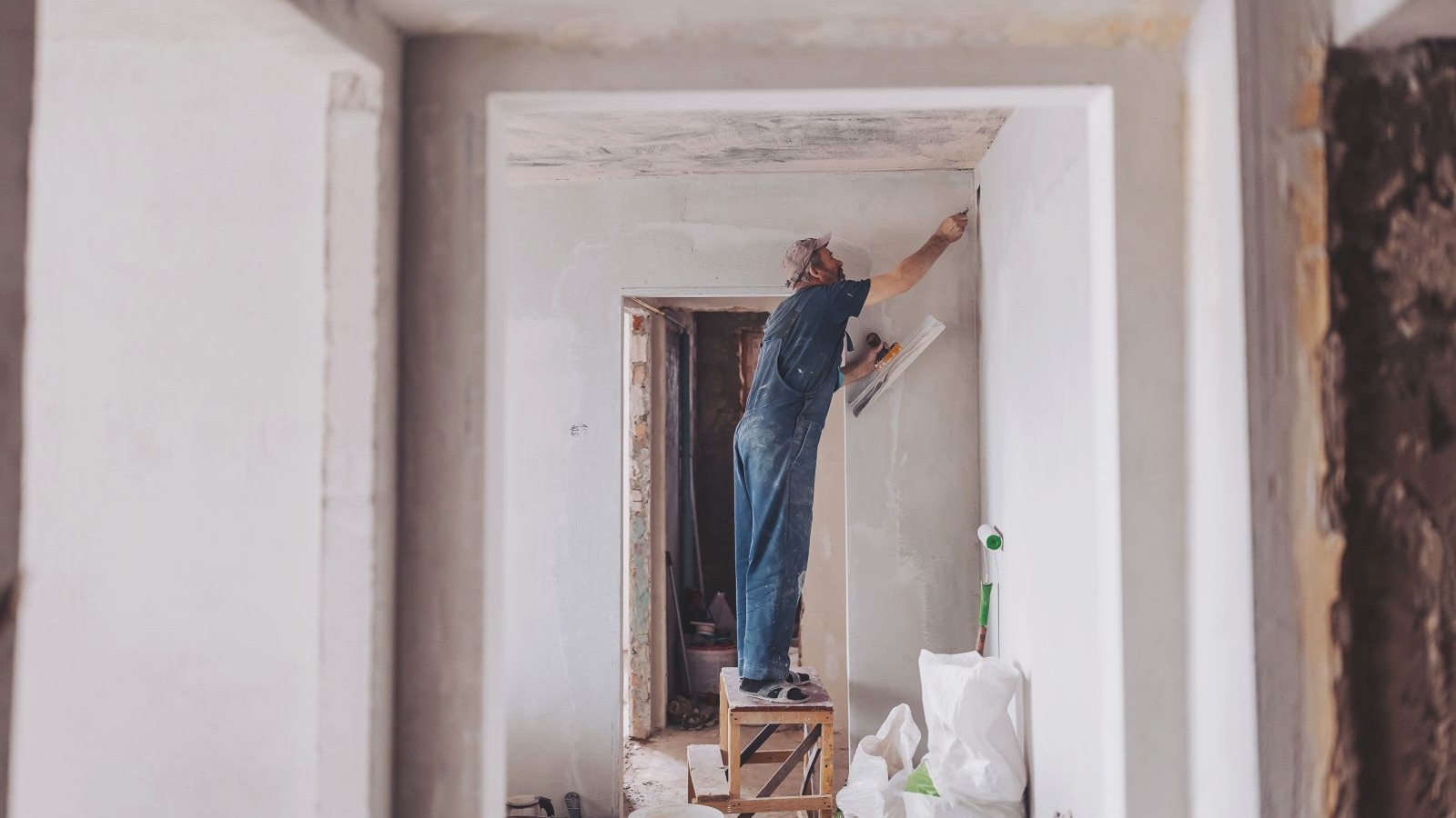 A man in blue dungarees on wooden steps plastering a wall