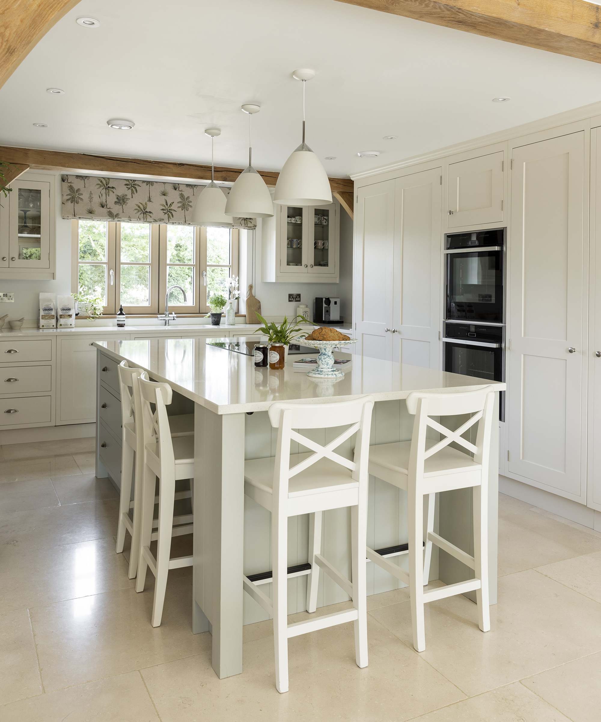 A neutral kitchen with light coloured flooring and cabinetry with central island and exposed beams