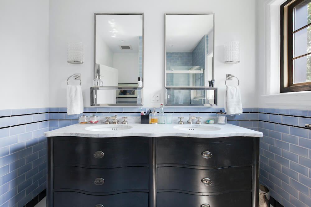 Black vanity below a double sink and double mirrors with blue half tiles in bathroom after renovation