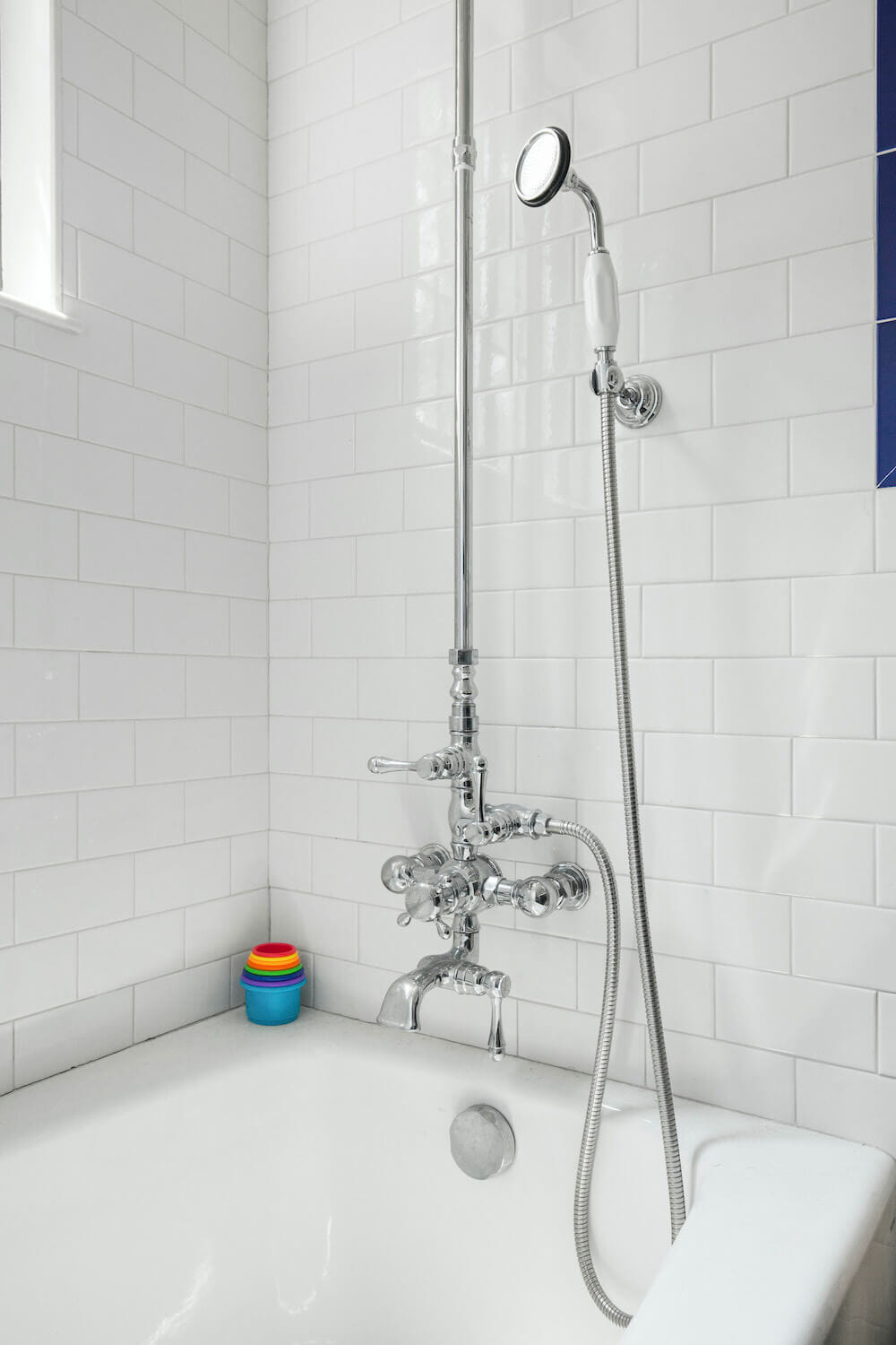 White bathroom tiles over a white bathtub with hand shower after renovation