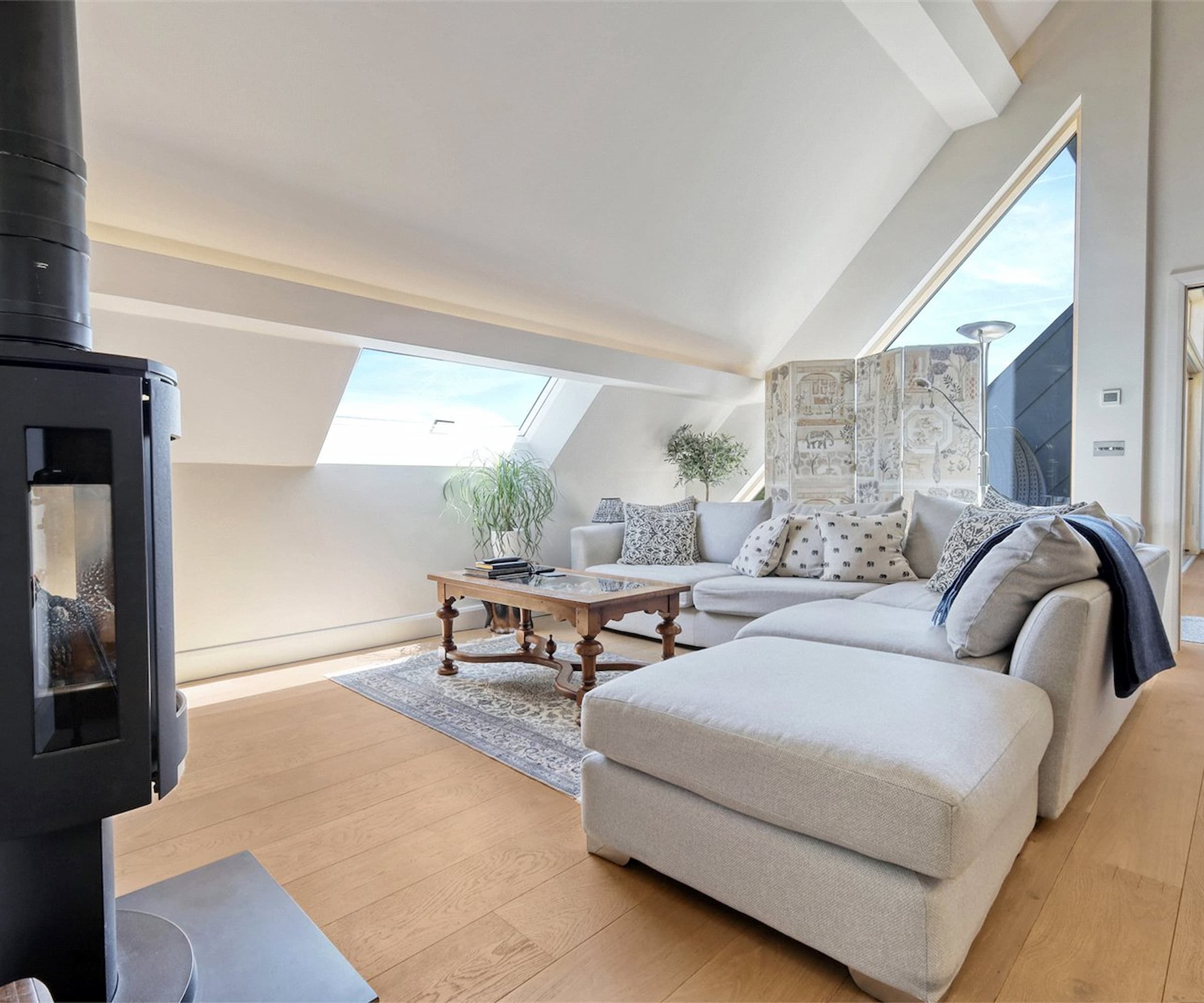 An upstairs living room with a woodburner and 90 degree sofa with a slanted roof