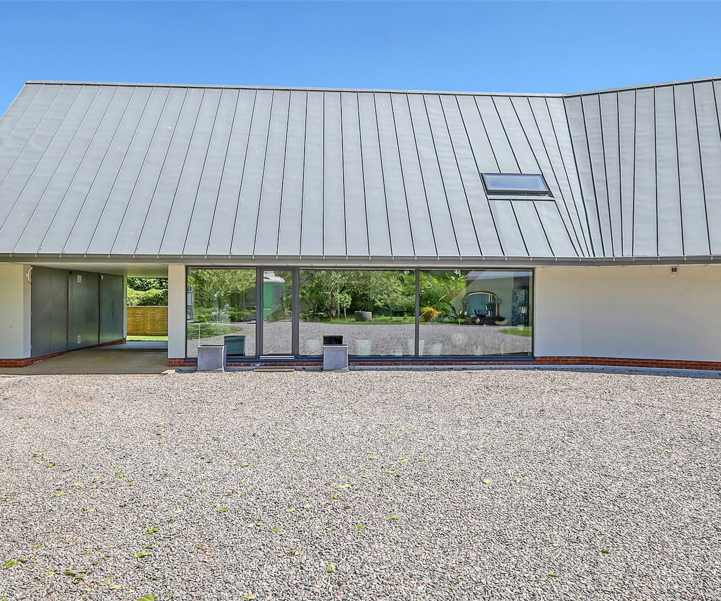 A gravelled driveway next to a grey house with tall glass bifold doors