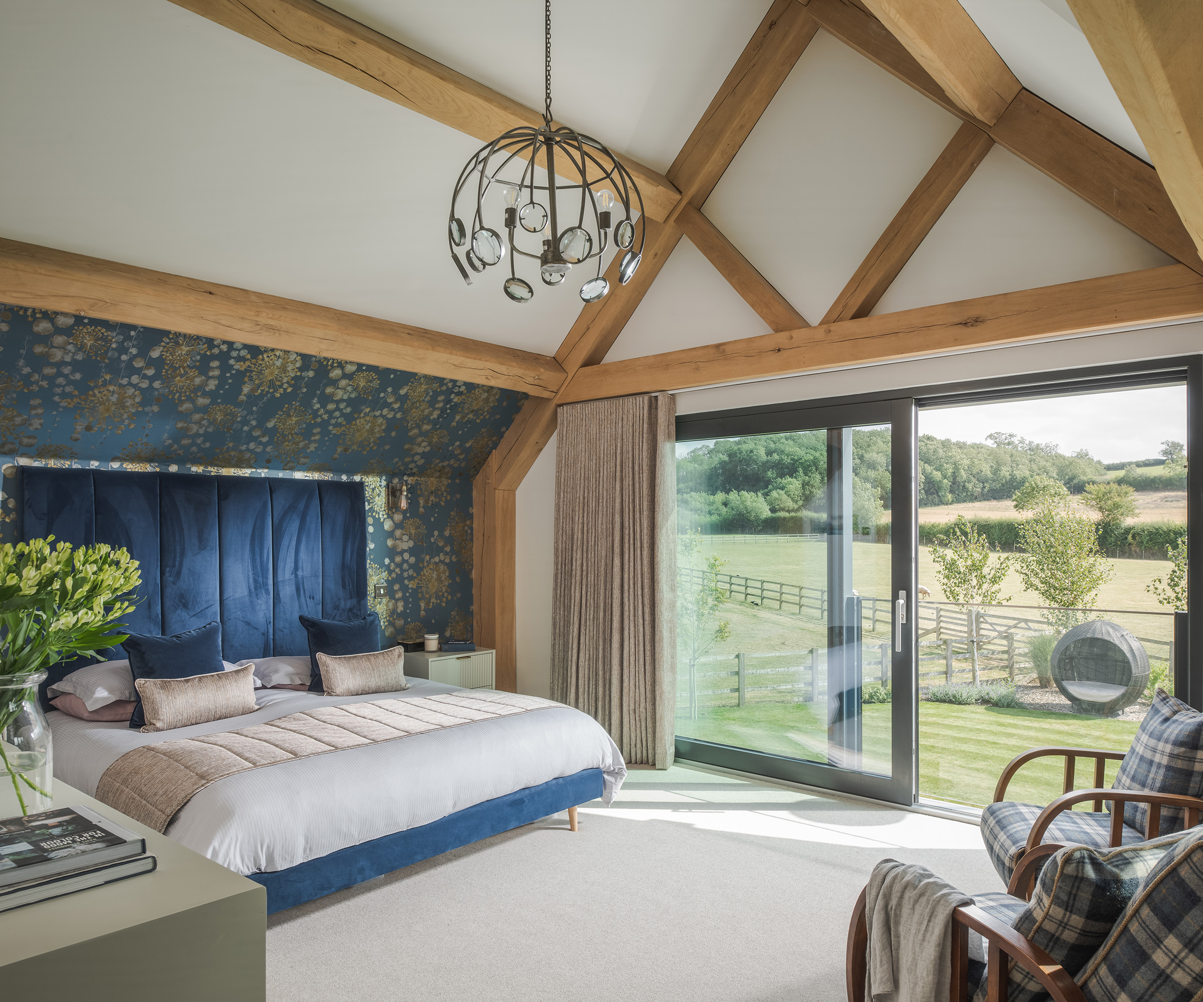 A double bedroom in a timber frame home with sliding doors looking out to countryside views