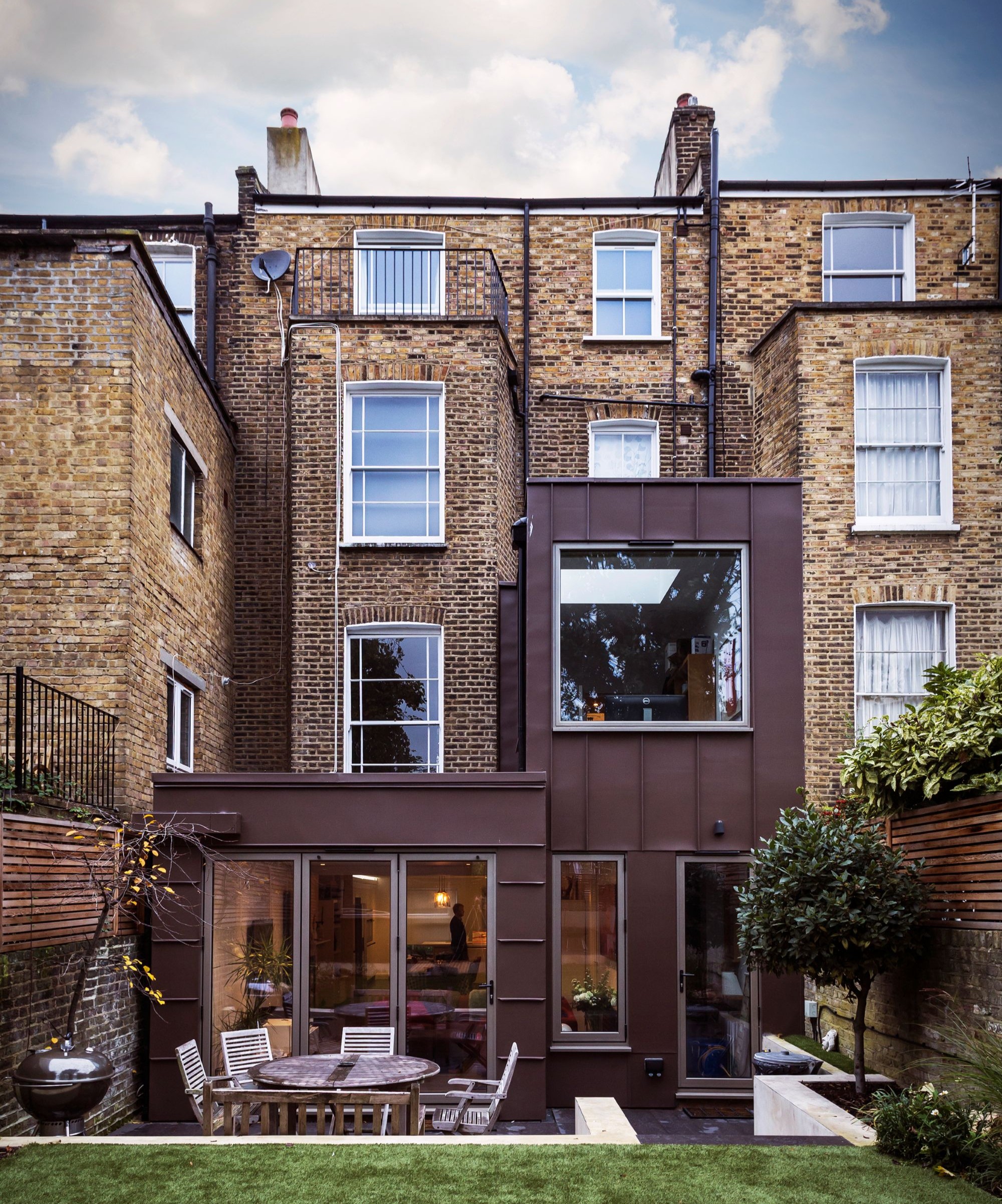 A brick four storey terraced home with a red metal clad two storey extension at the rear