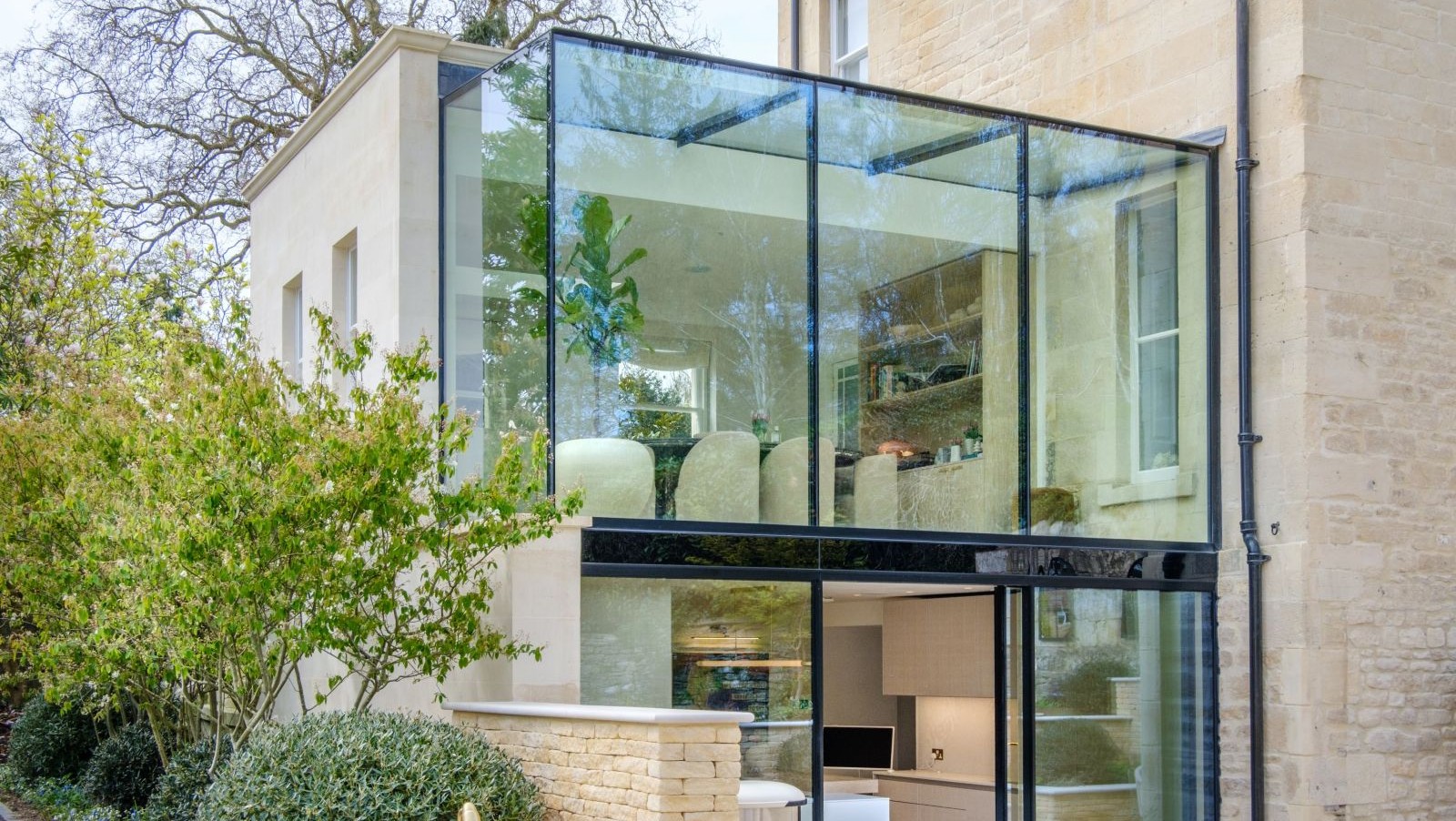 A glass extension with black metal framing and buff coloured brickwork on the original building