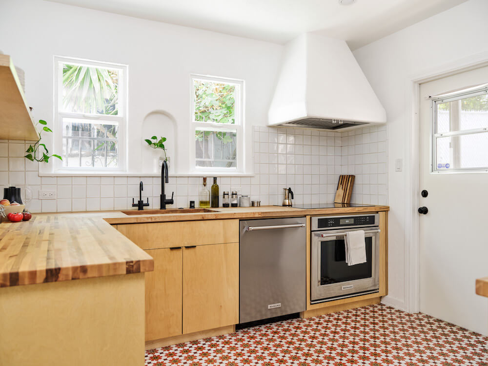 white kitchen with patterened floor tiles and golden oak cabinets and butcher block countertop and range hood after renovation