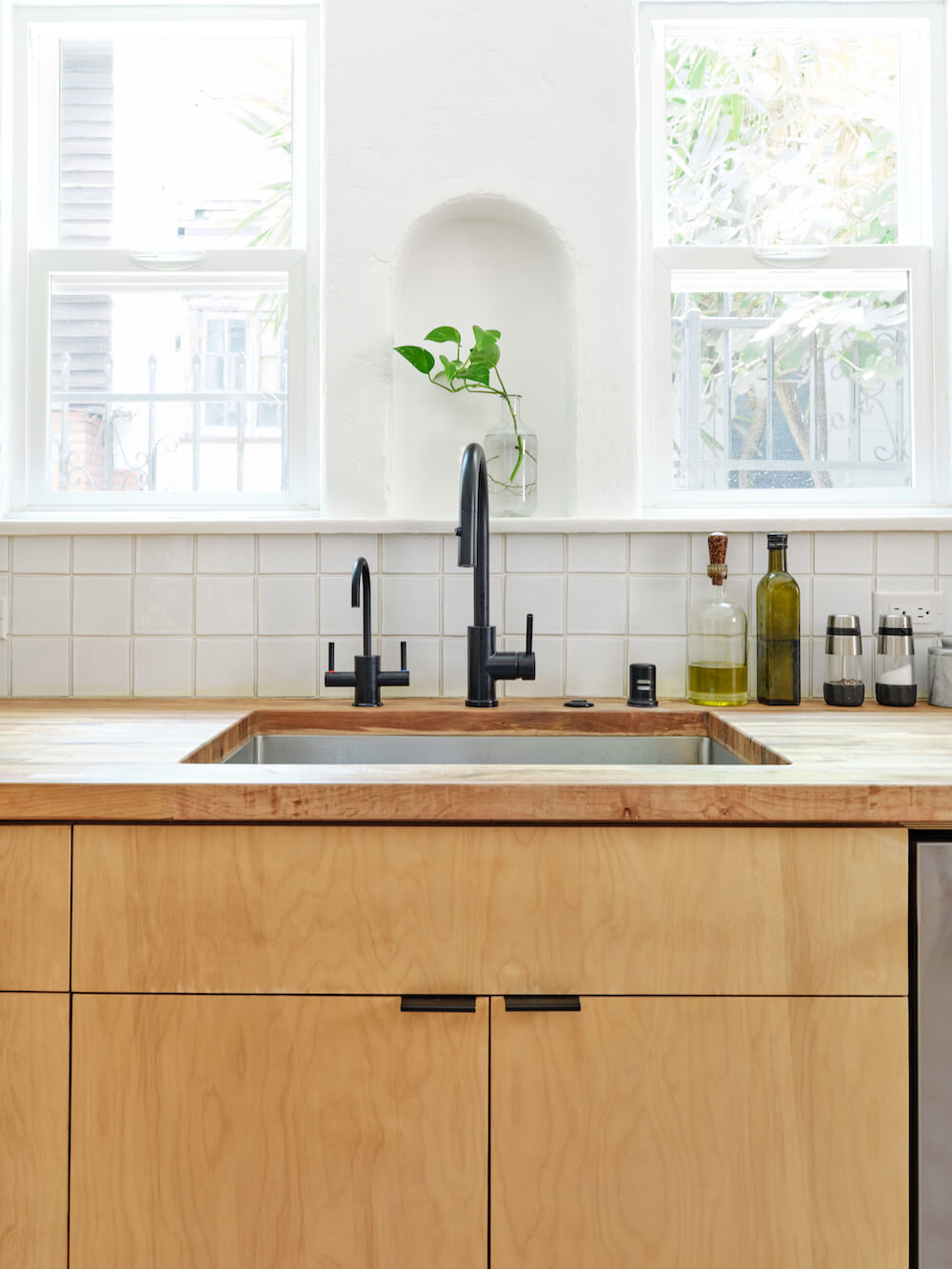 kitchen windows over undermount farmhouse sink with black faucets and wooden countertop and white backsplash tiles after renovation