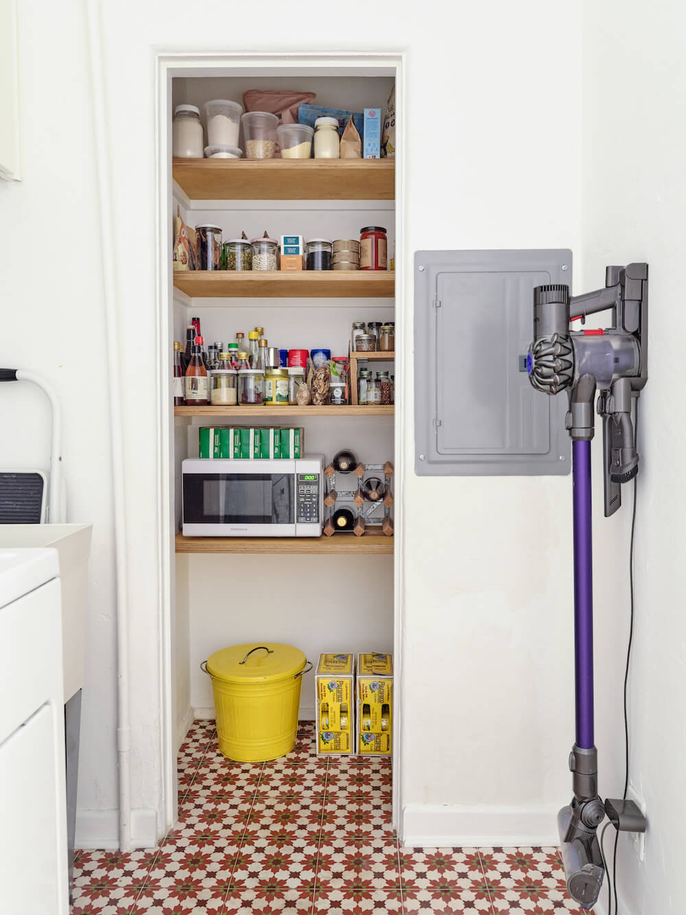 small pantry storage with wooden shelves and geometric patterned tiles after renovation