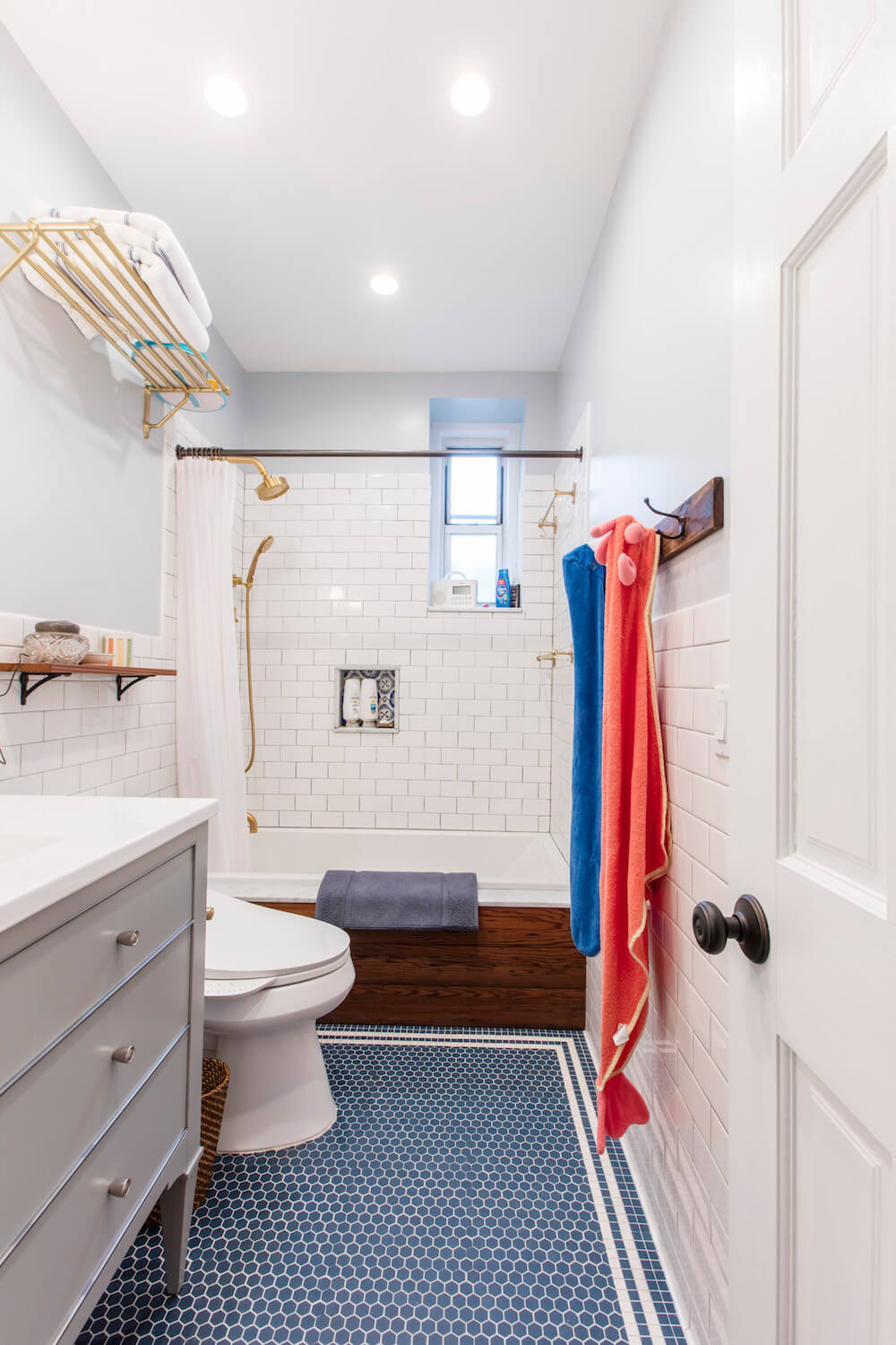 White door with knob opening to white bathroom with blue penny tiles with white vanity and white tub after renovation