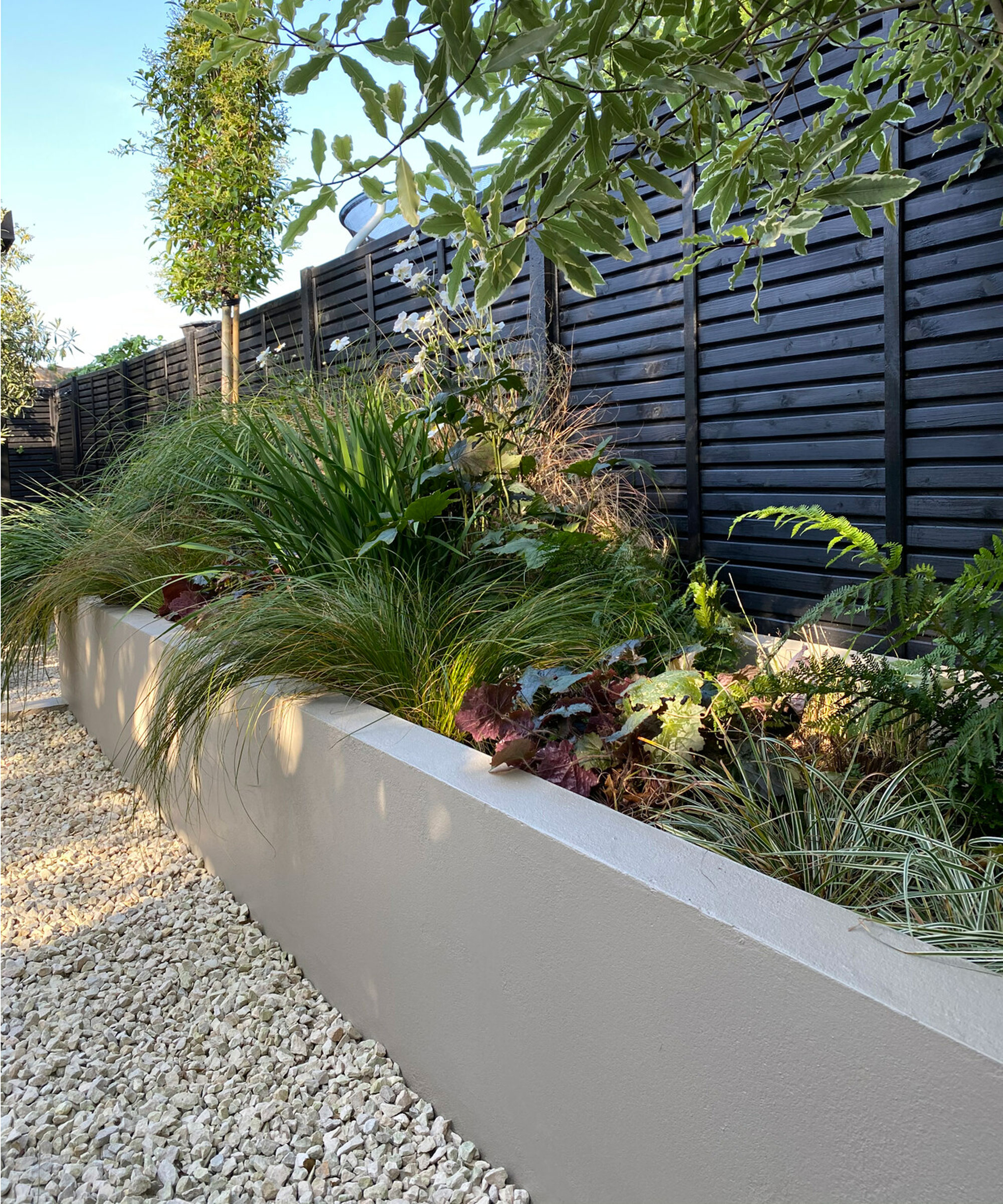 raised bed with planting, black slatted fence and gravel driveway in front garden design