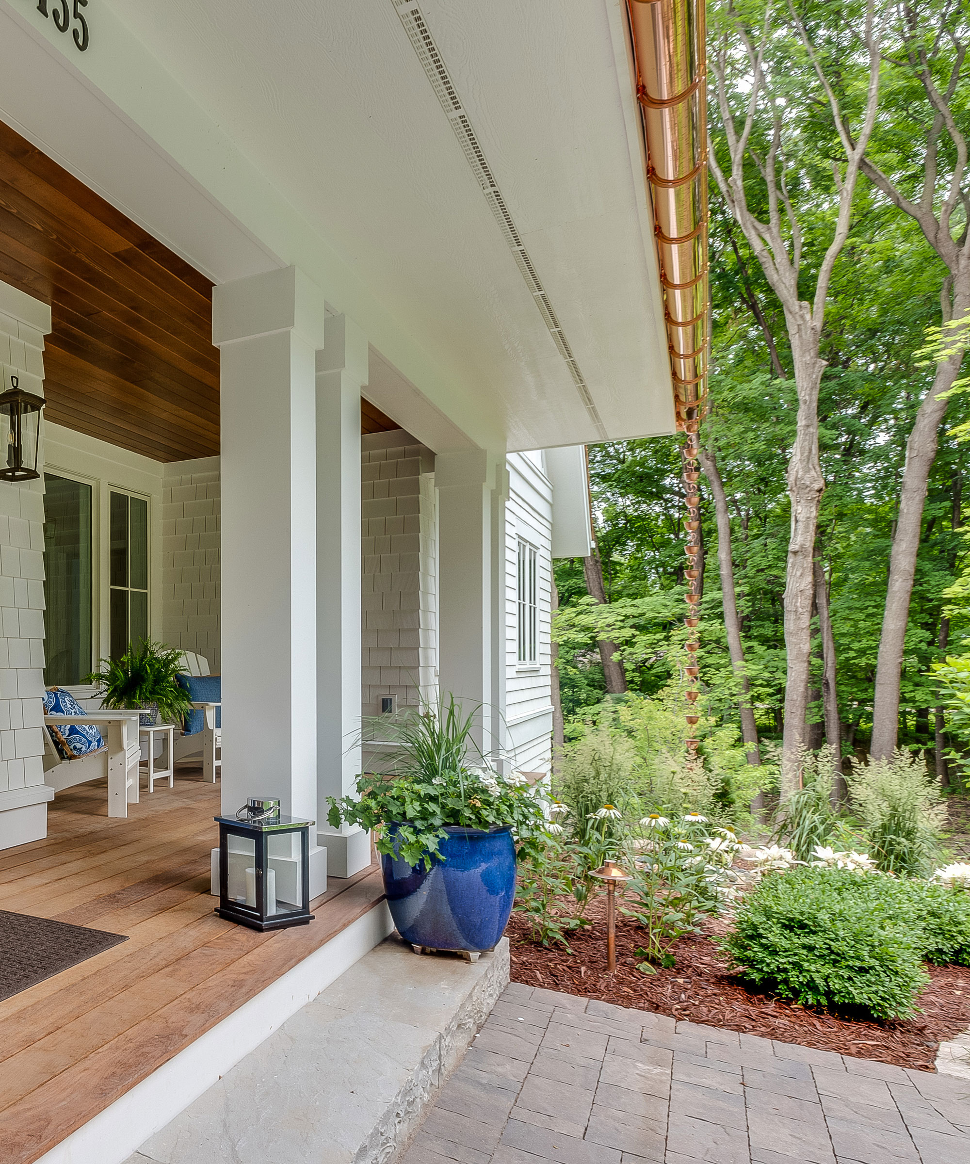 veranda of house with furniture and lanterns, with copper guttering and copper rain chain, flowerbeds and trees
