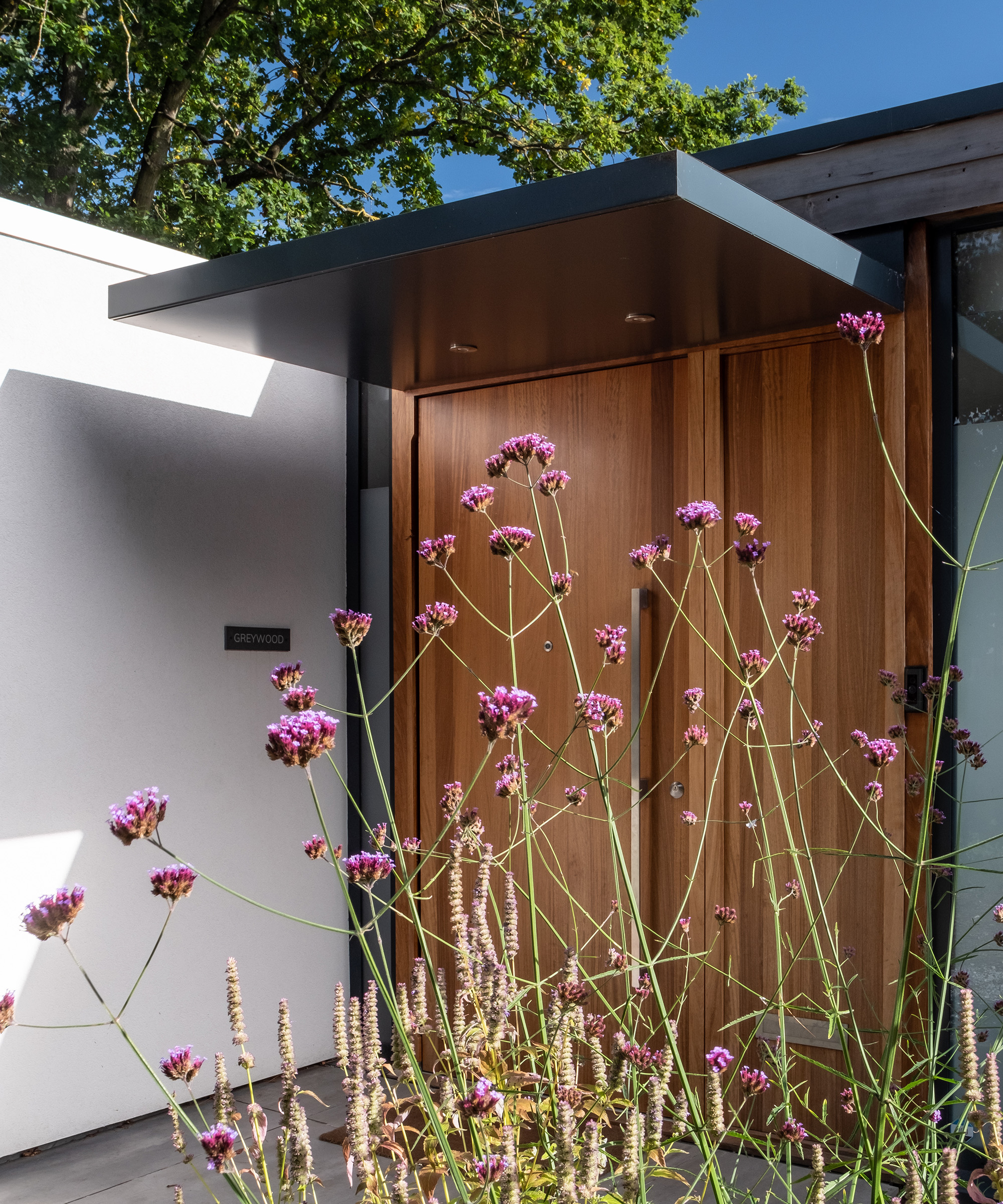 A modern timber front door of a self build home with some flowering herbs in front of  the door