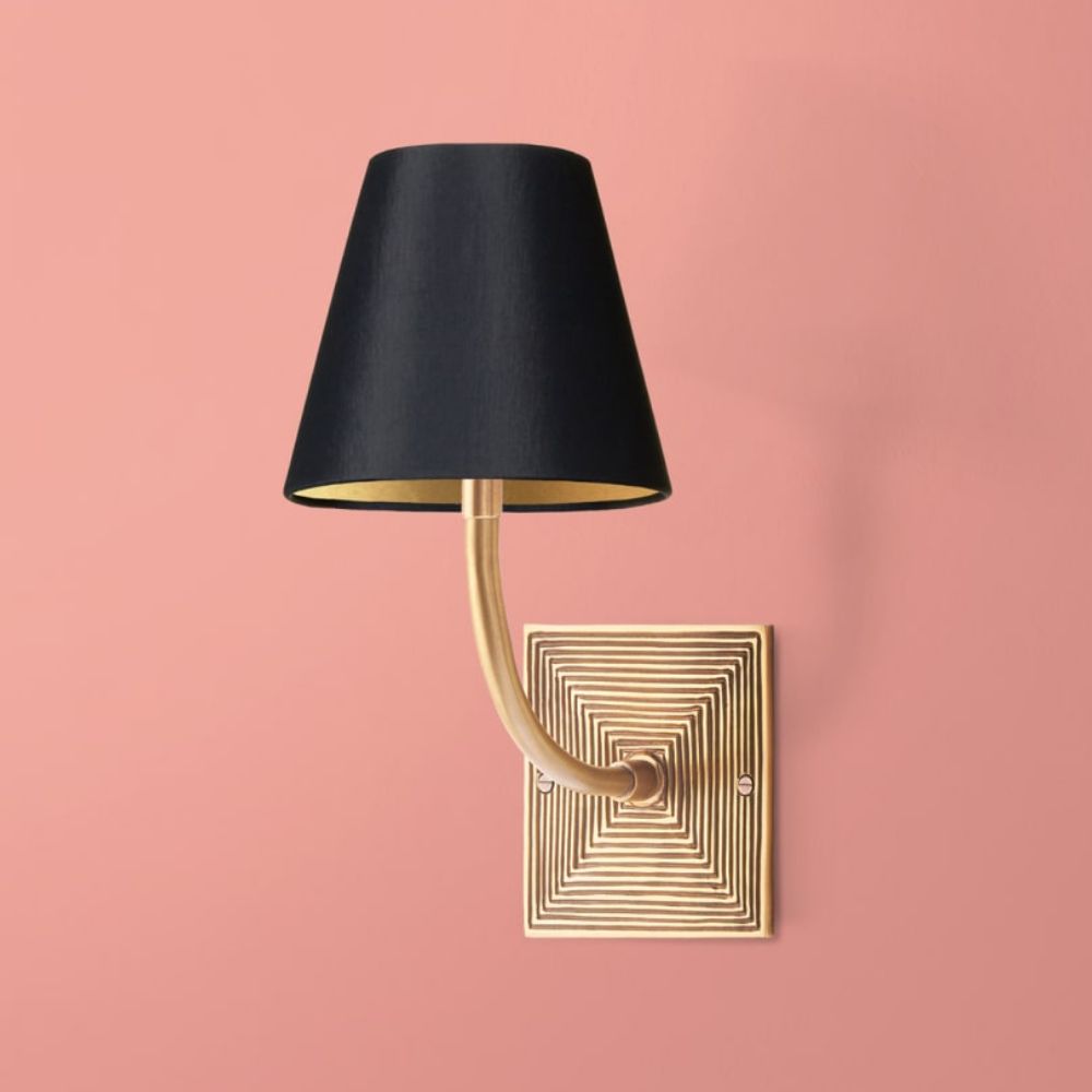 A brass wall sconce in antique brass with a black shade