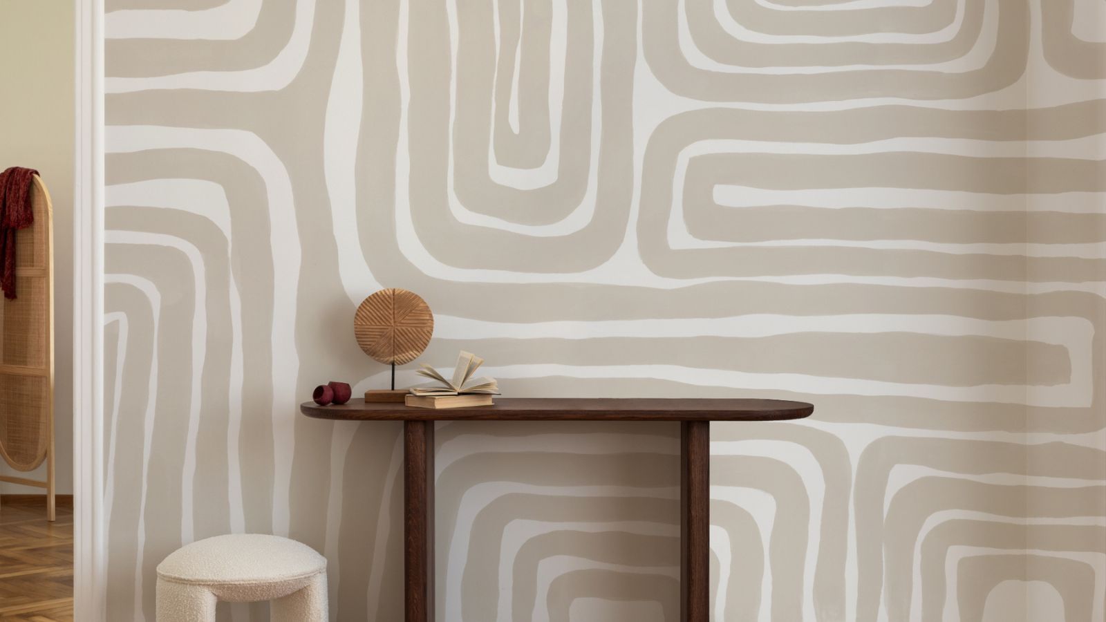 Beige and white abstract wallpaper with wide, wavy stripes behind a slim dark wooden console table.