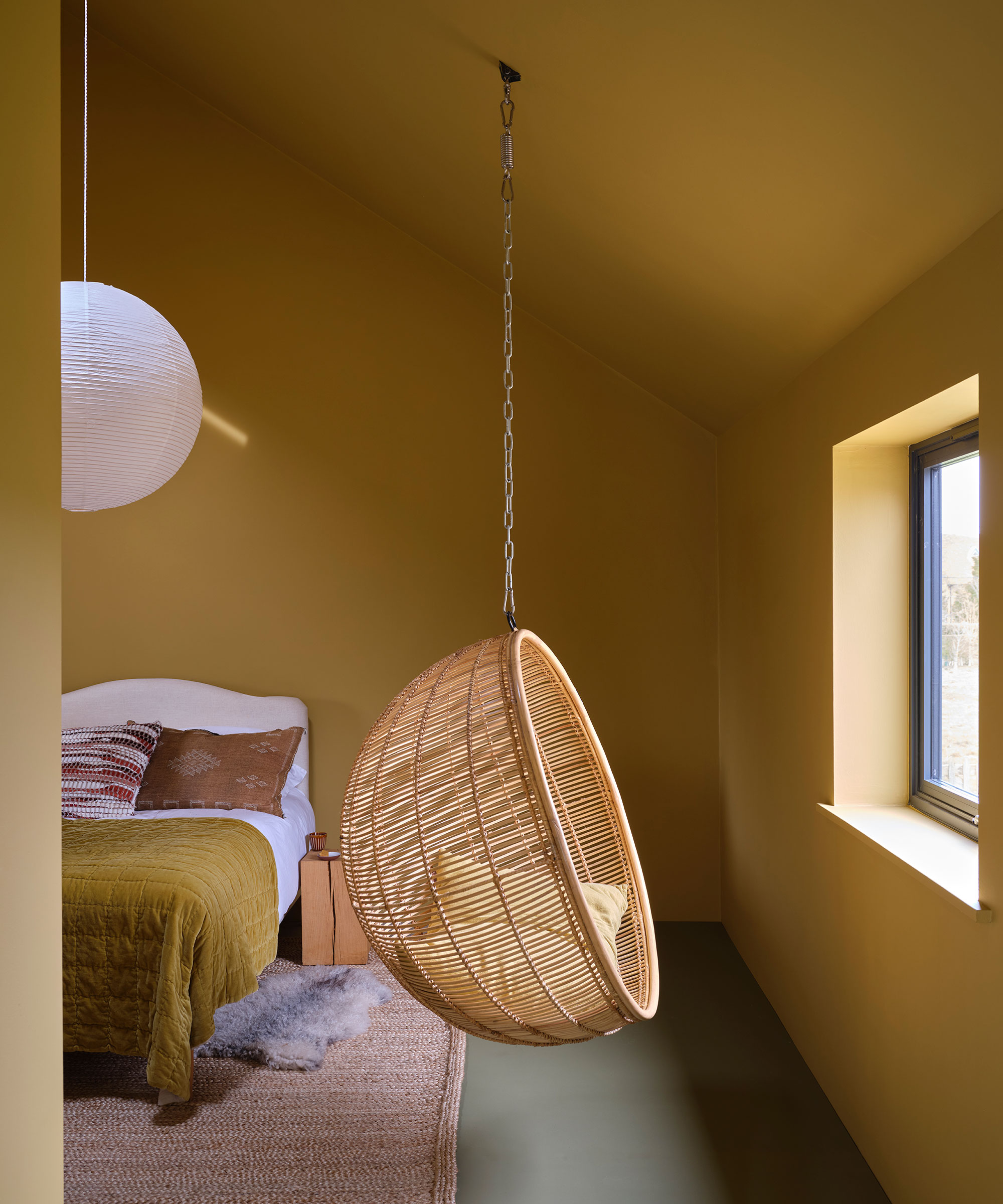 yellow bedroom painted in Farrow &amp; Ball paint with a wicker hanging chair
