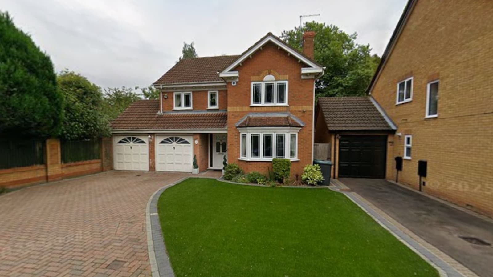 The front of a semi-detached brick home and small grass garden with double garage