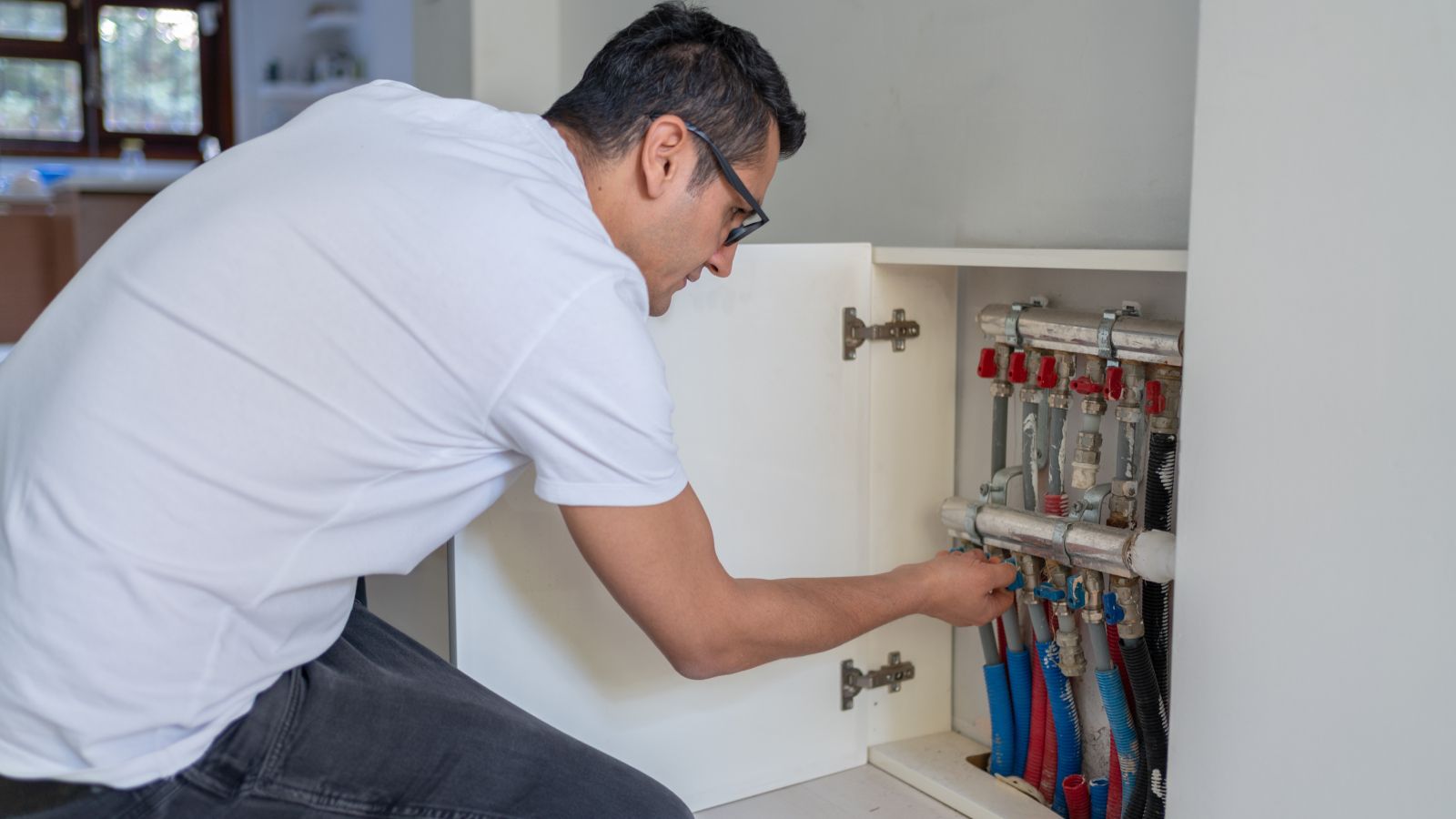 man looking at underfloor heating manifolds in cupboard
