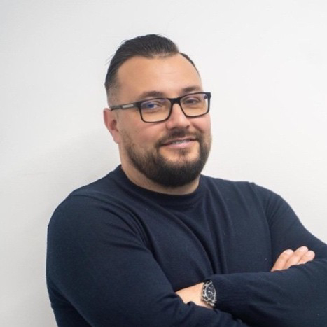 male with short black hair and beard wearing glasses and navy sweatshirt