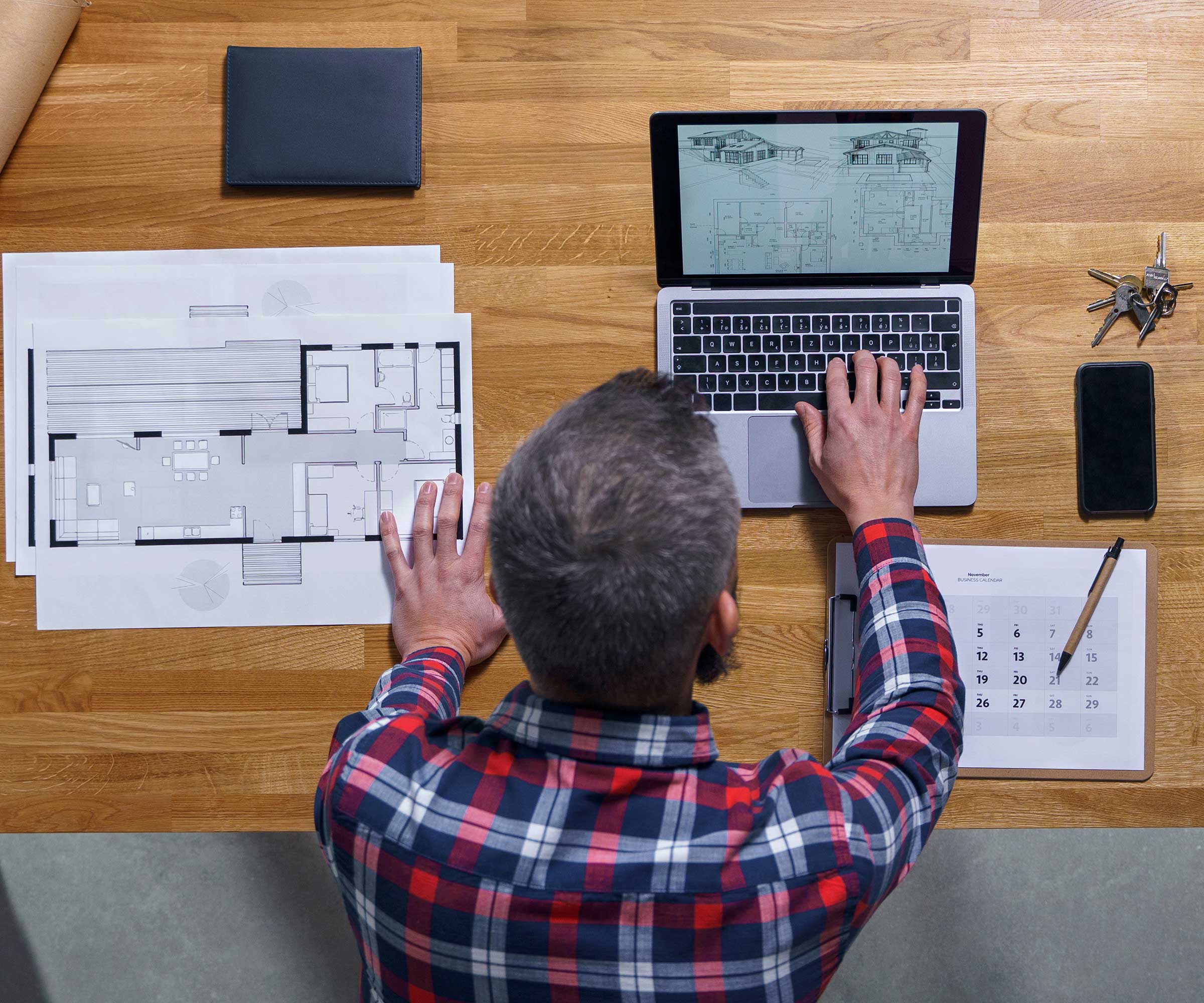 person sitting at a desk working on a laptop with architectural floorplans on the desk next to the laptop