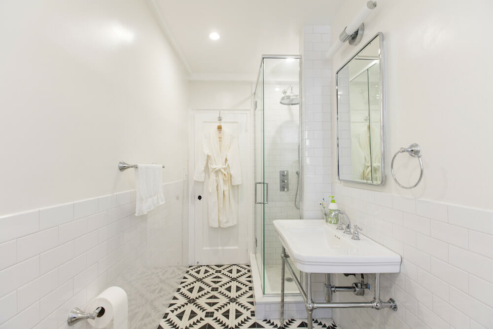 A stylish, clean bathroom with a glass shower, white tiles, and a geometric patterned floor.