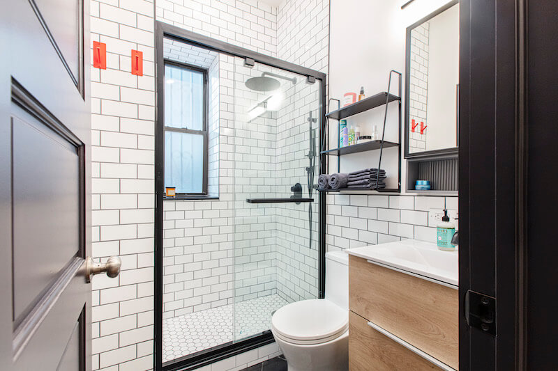 A bathroom with a framed glass shower door, subway tiles, and a contrasting black and white floor pattern.