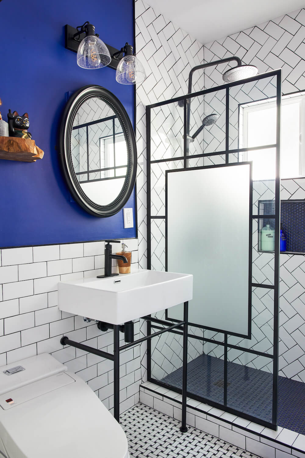 A modern bathroom with a geometric tile floor, tinted glass shower door, and a stylish blue accent wall.