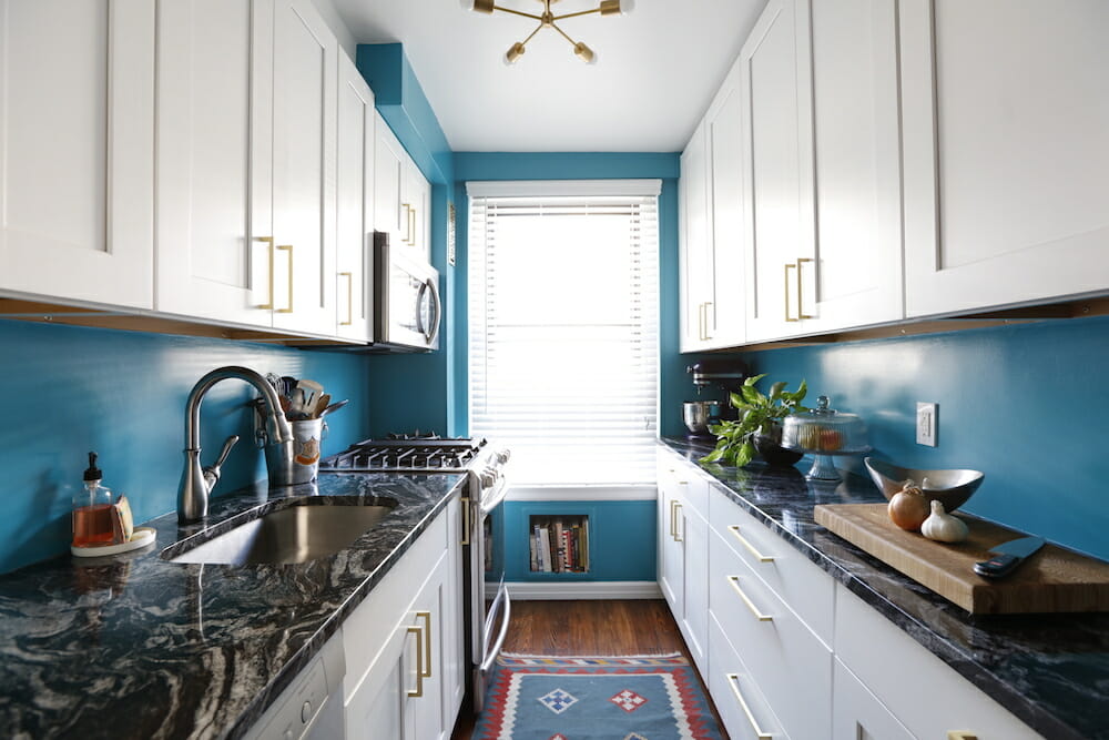 Blue-walled galley kitchen with white shaker cabinets and dark stone counters.