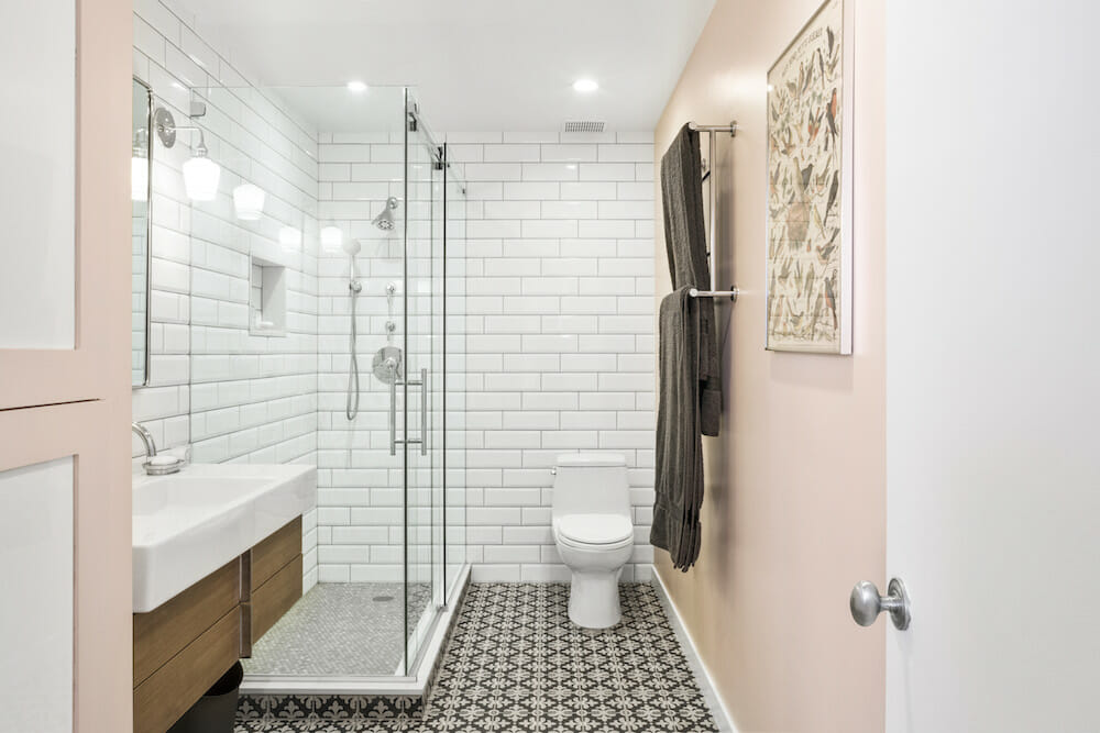 glass shower enclosure A modern bathroom with a glass shower door, white subway tiles, and bold patterned floor tiles.