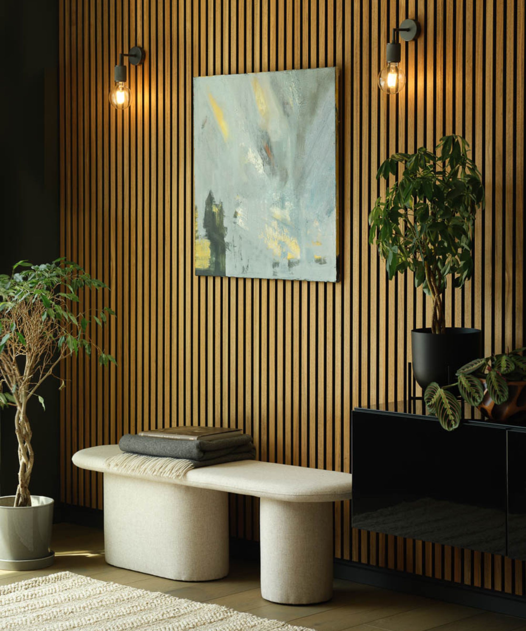 A warm, contemporary hallway featuring oak slatted wall panels and soft ambient lighting. A minimalist cream bench and indoor plants add texture and calm, while abstract art provides a modern focal point.