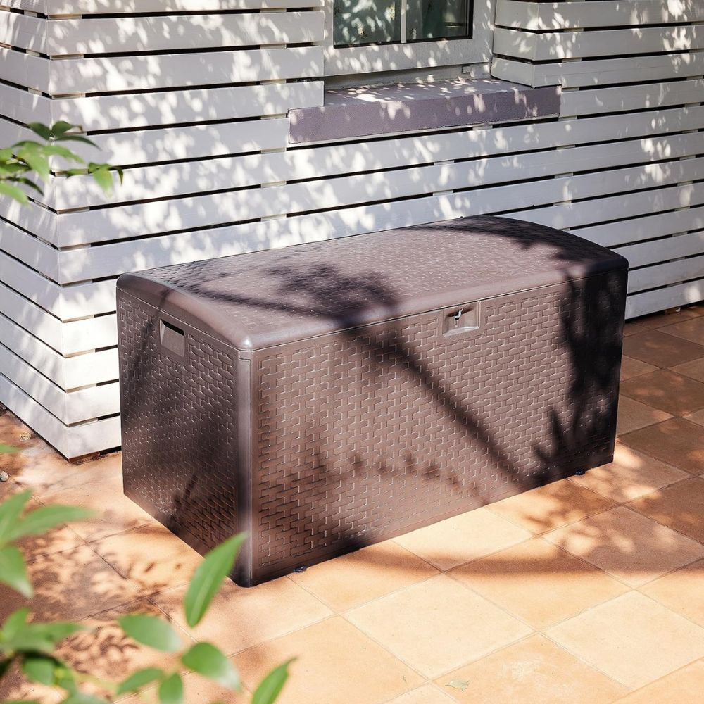 Brown wicker-style outdoor storage box placed on a tiled patio beside a white wooden wall.