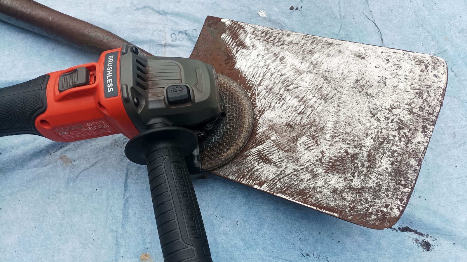 Black + Decker Cordless Brushless Angle Grinder sat on top of newly cleaned rusty garden spade on blue dust sheet