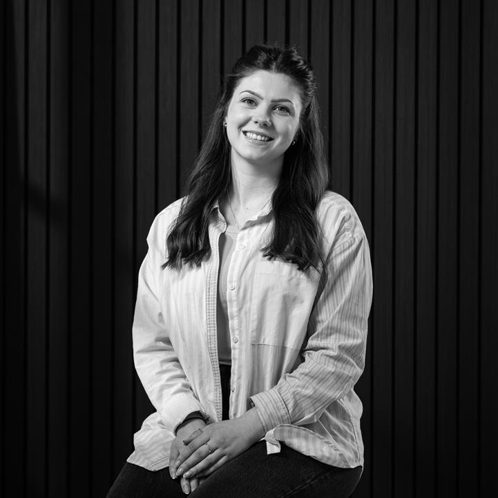 female with long dark hair wearing light shirt sat on stool with panelled wall behind