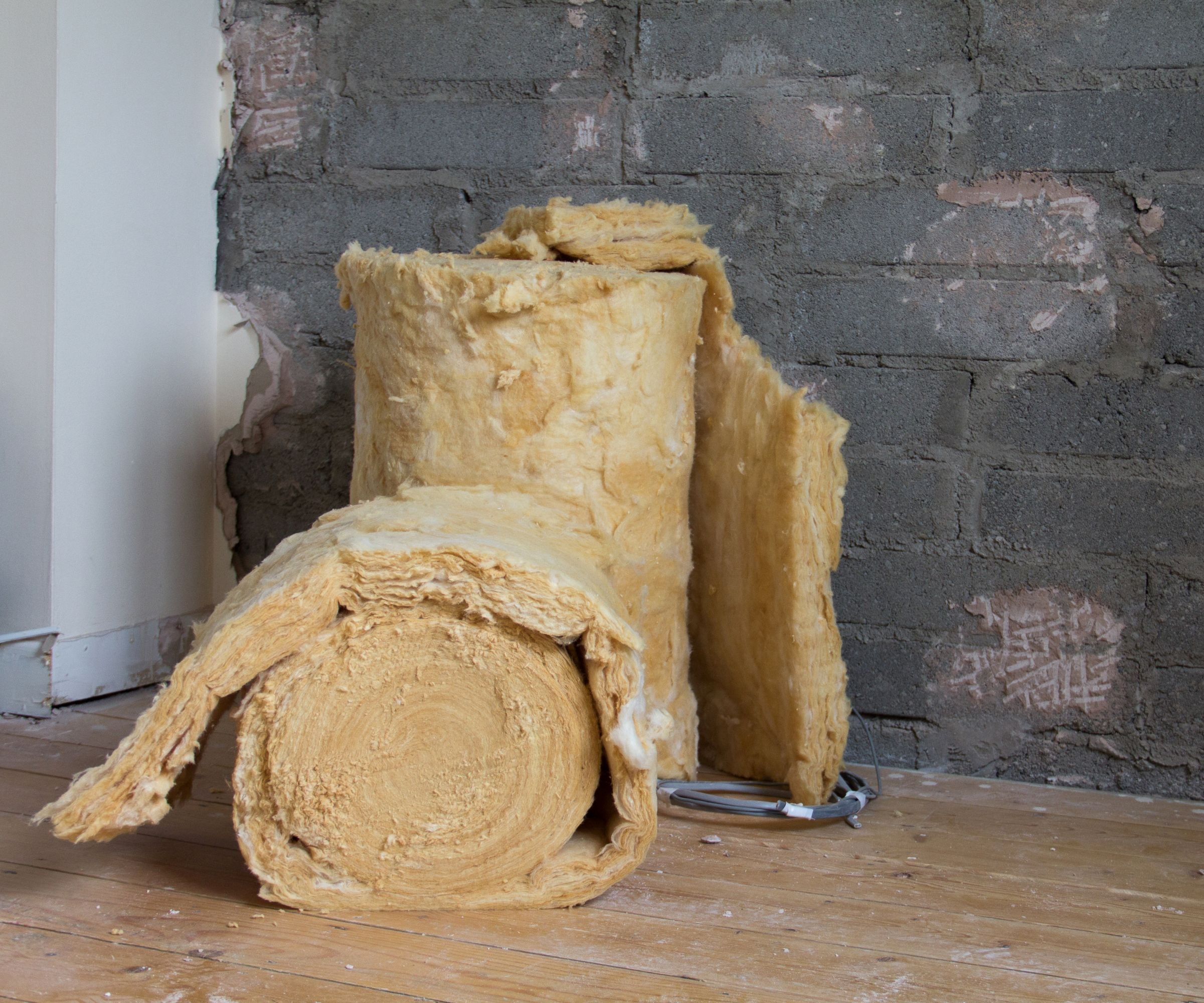 Rolls of insulation on a wooden floor beside a grey wall