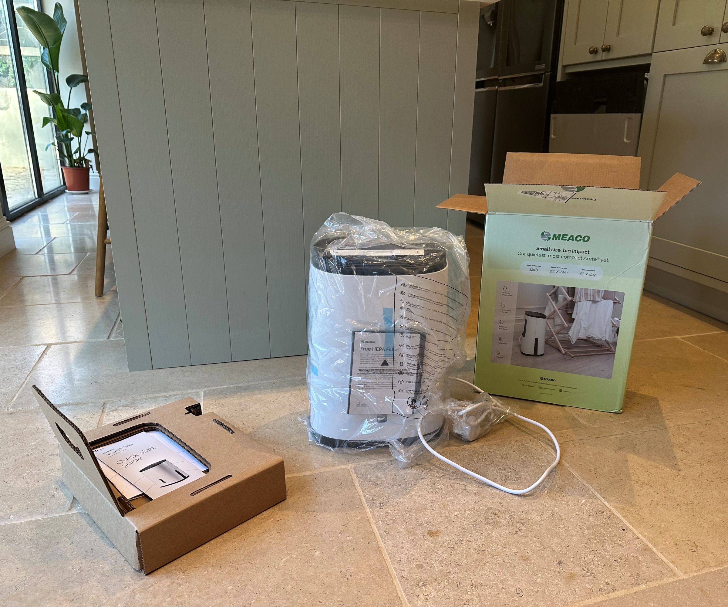 The MeacoDry Arete One 6L Compact dehumidifier being unboxed in a kitchen with green units and a limestone tile floor