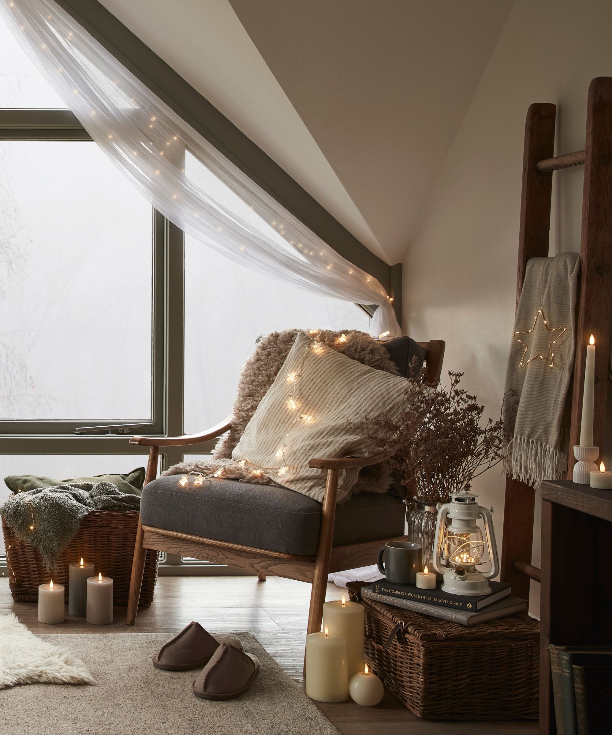 A peaceful attic reading spot with a wooden armchair, soft blankets and cushions. Fairy lights, candles and wicker baskets add warmth, while a large window draped in sheer fabric brings gentle natural light into this serene, comforting corner.