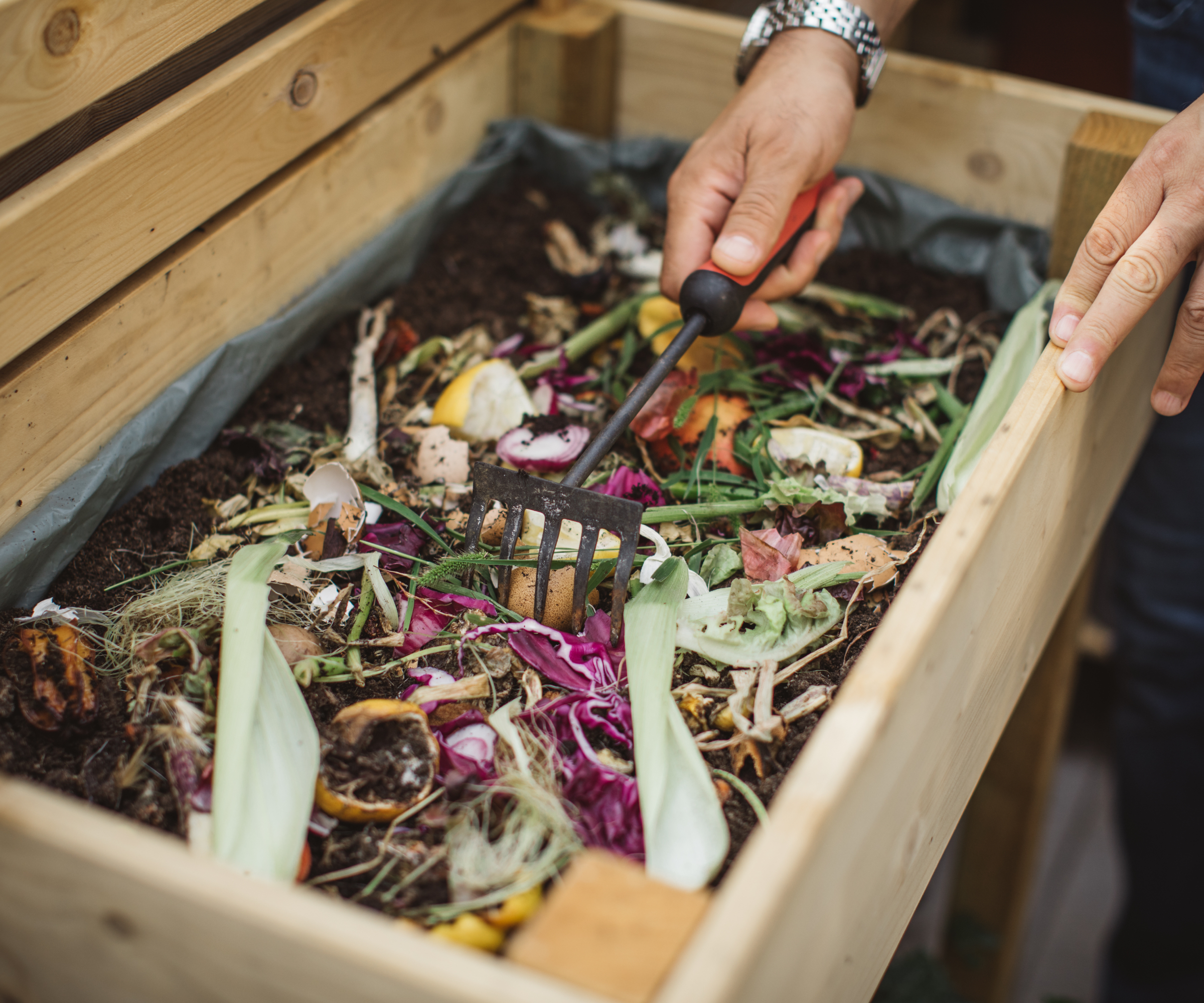 Wooden compost bin filled with garden waste and vegetable leaves being raked over
