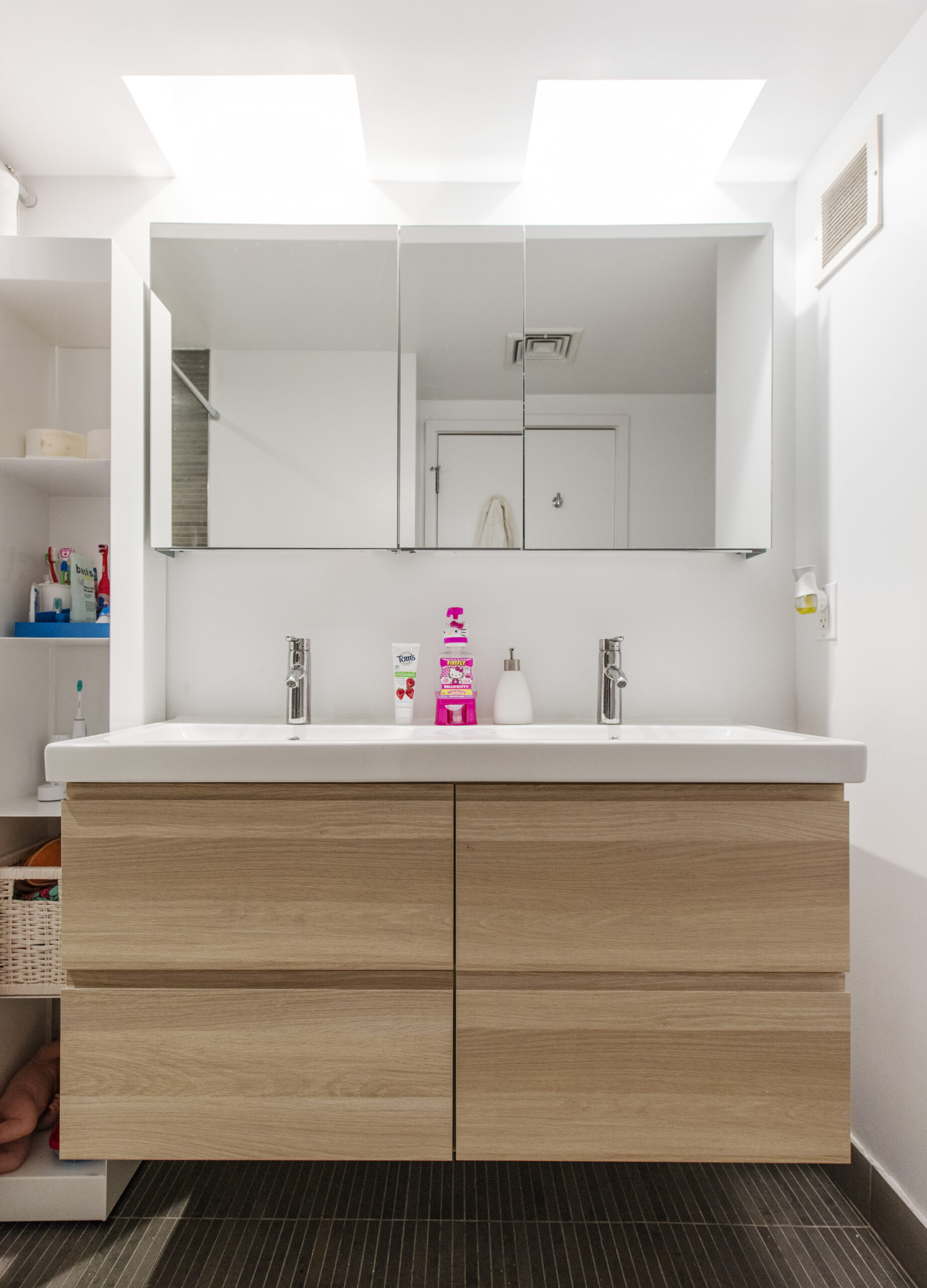 A refreshed bath with a light oak bathroom vanity, wide integrated sink, twin faucets, and mirrored medicine cabinets.