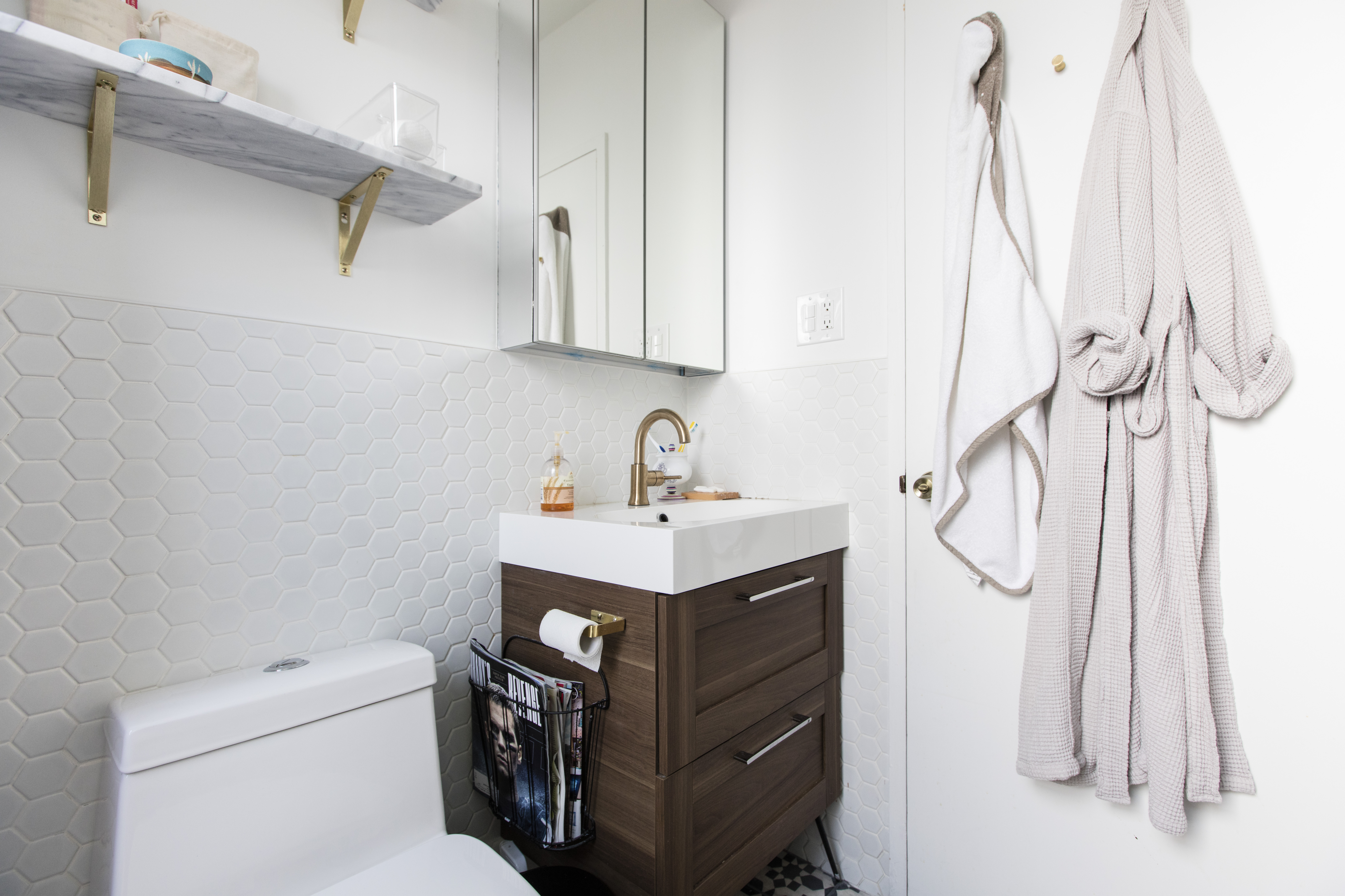 A redesigned bath with a compact bathroom vanity, crisp white sink, brass faucet, and hex tile wainscoting.