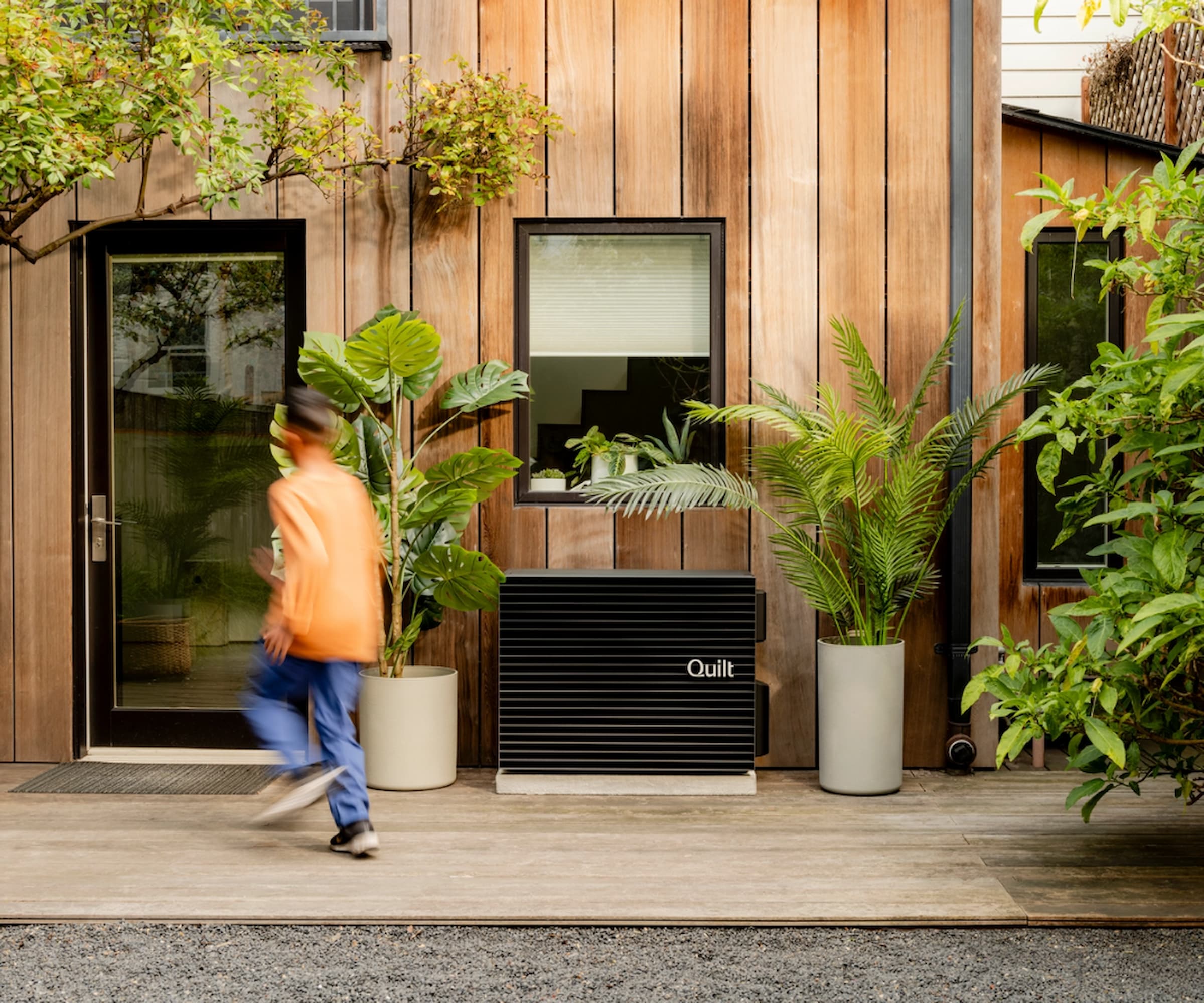 A Quilt outdoor heat pump on house with wooden cladding, grey aluminium framed windows and doors and plants outside