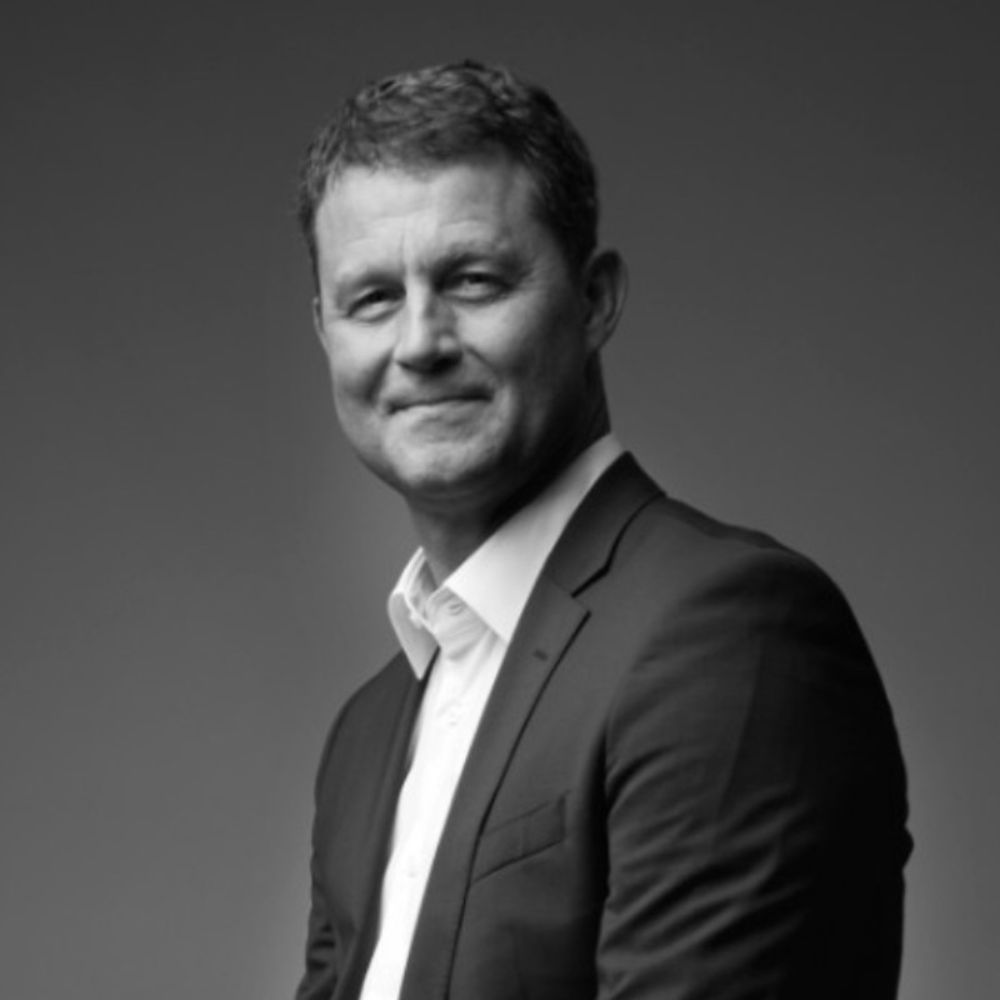 Black and white headshot of a man in a suit against a grey background